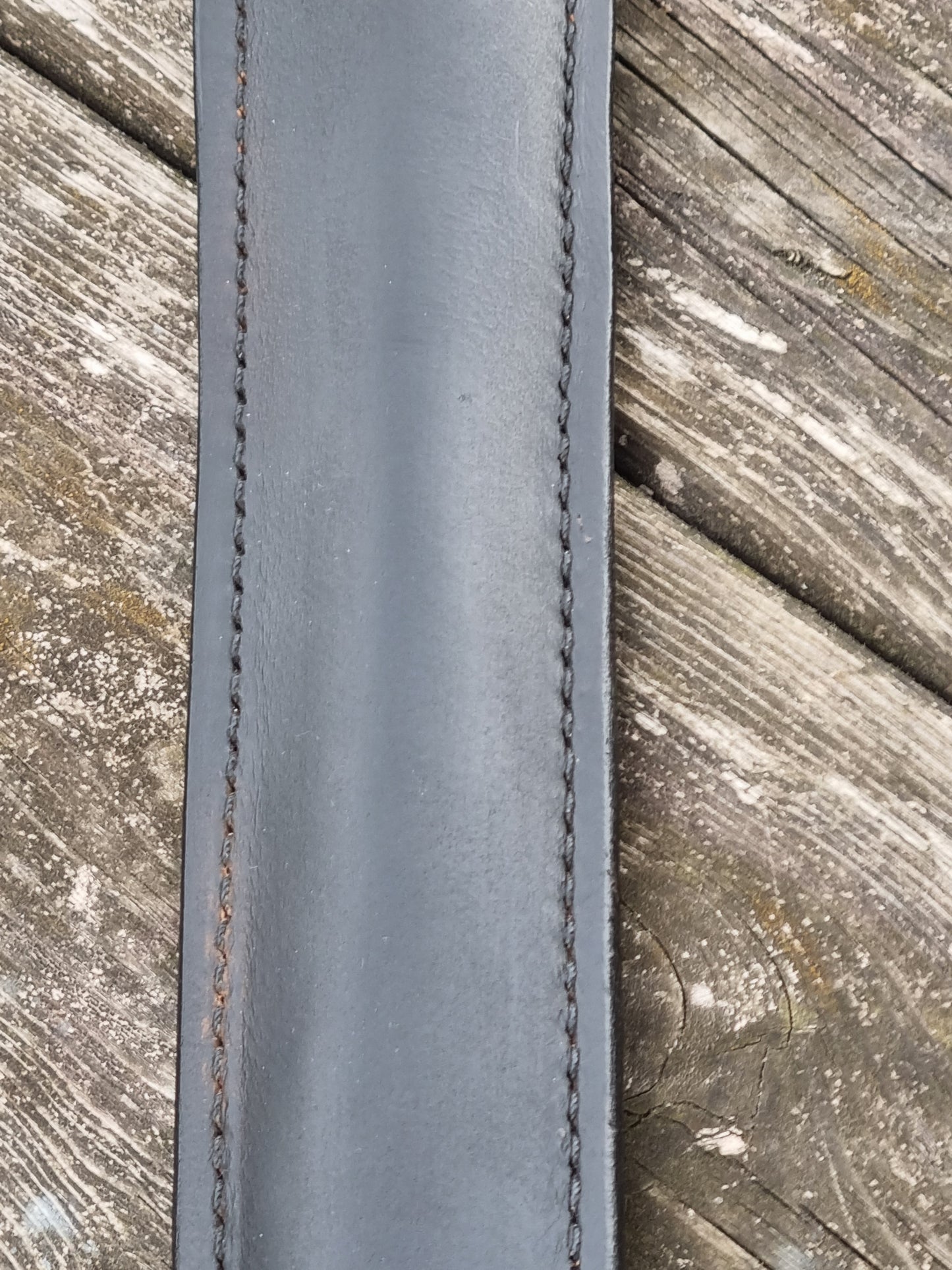 Showing close view of black leather sheath with stitching on a wooden surface