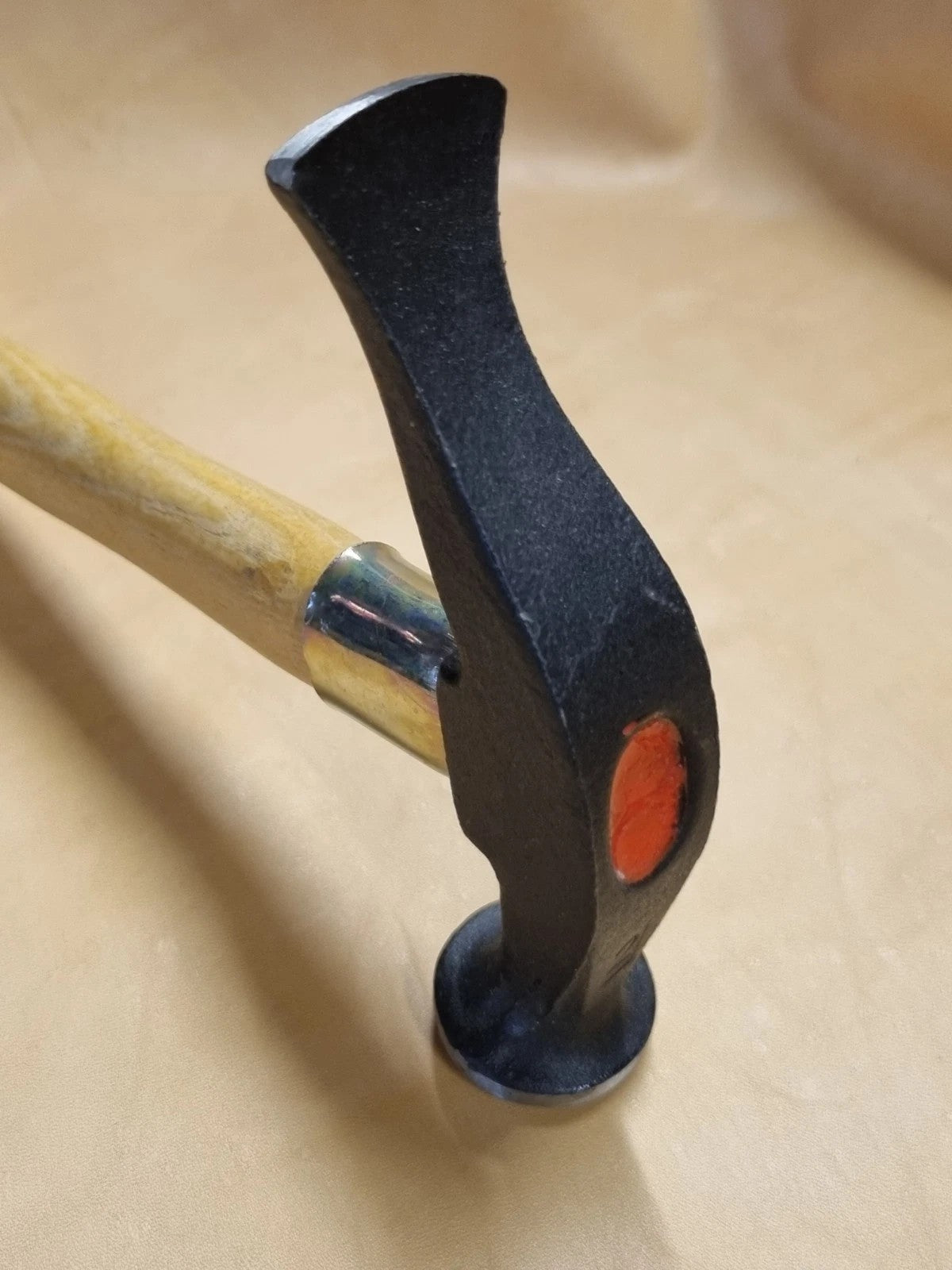 A close-up of a view of French hammer with a black metal head and a light wood handle, resting on a beige surface.