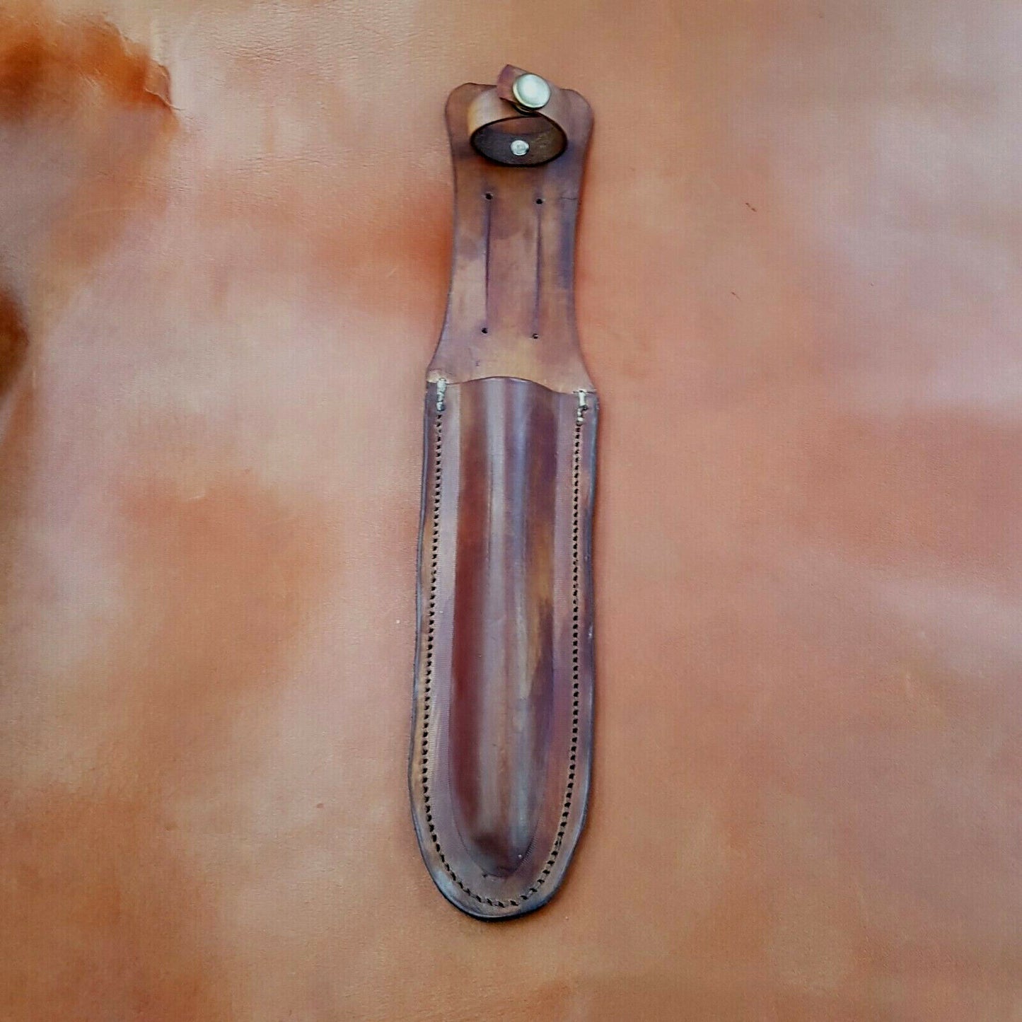 Brown leather sheath for a Hori-Hori gardening knife, hand moulded and saddle stitched, displayed on a textured background.