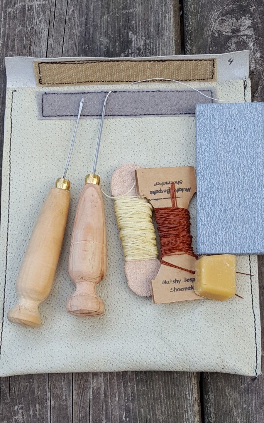 The image shows a cobbler's awl kit with two types of awls plus waxed threads, patching thread, and fine emery paper, neatly arranged on a tool bag