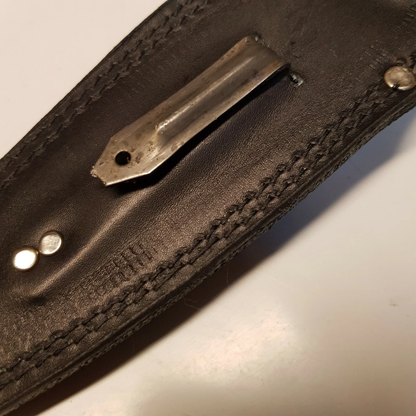 Close view of black leather Pentagon SOG sheath showing back of the sheath with metal boot clip on white background