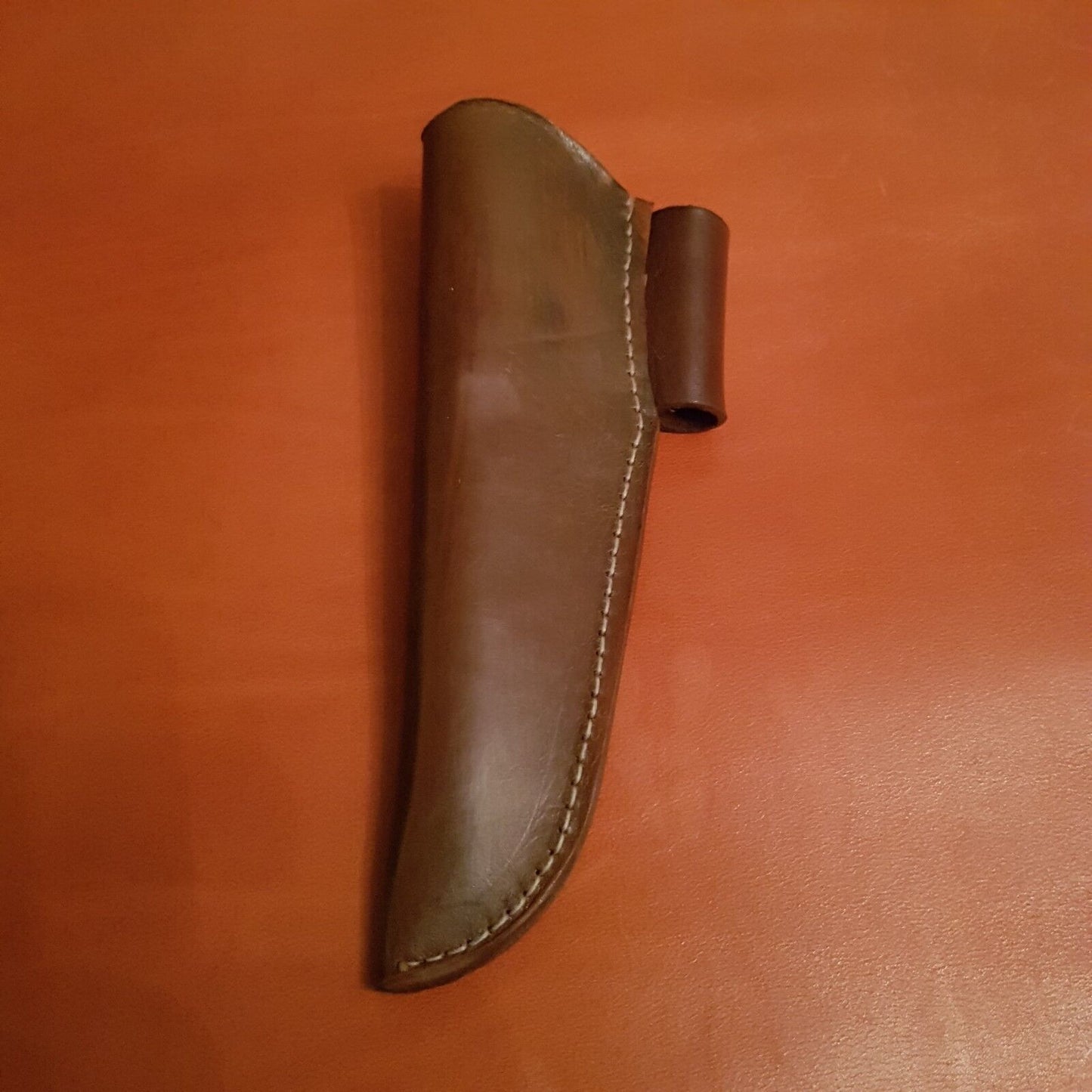 A brown leather sheath for a Morakniv 860 type knife showing fire steel loop on wooden background