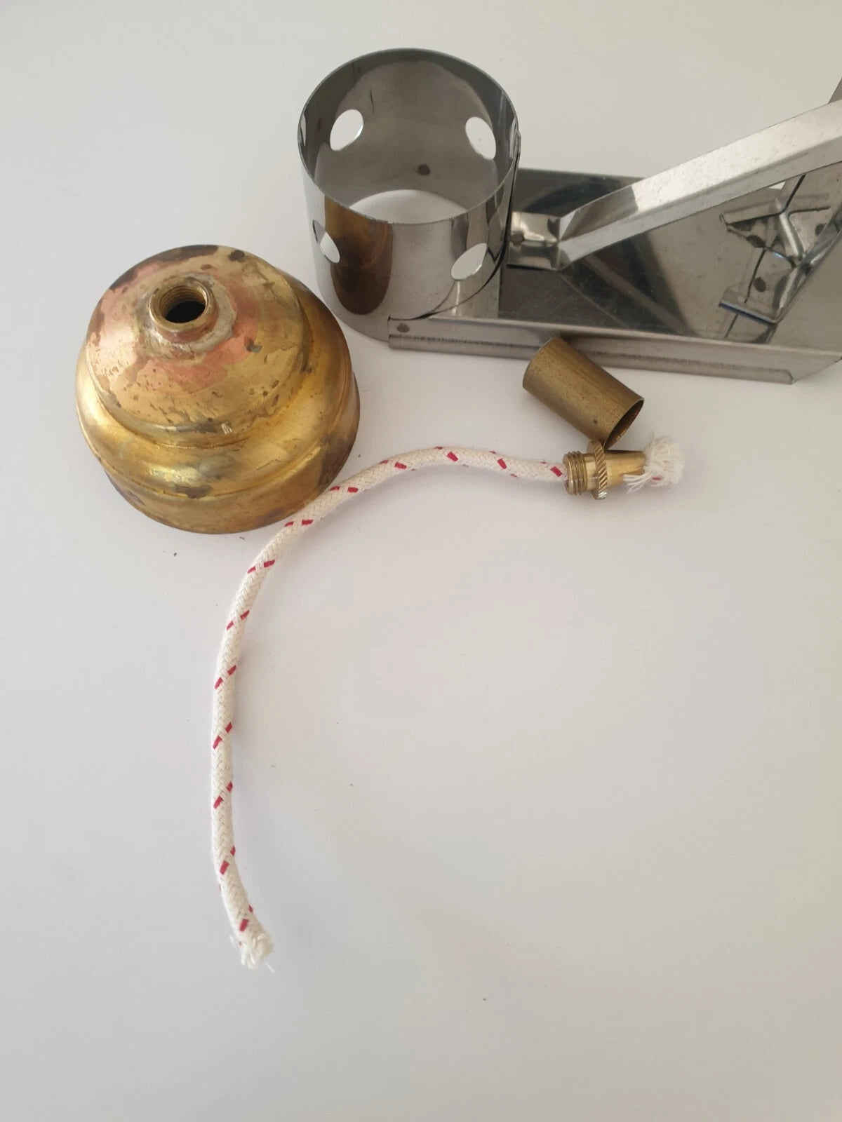 A portable shoemakers spirit lamp with a brass fuel can, a stainless steel stand, a brass nozzle, and a white wick with red markings, laid out on a plain white surface.