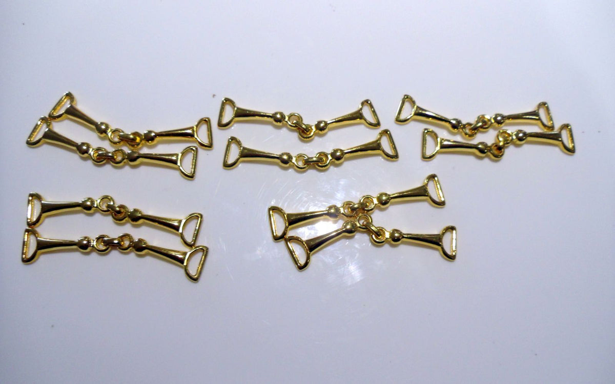 A collection of eight gold-colored metal moccasin trims arranged in two rows on a light background.