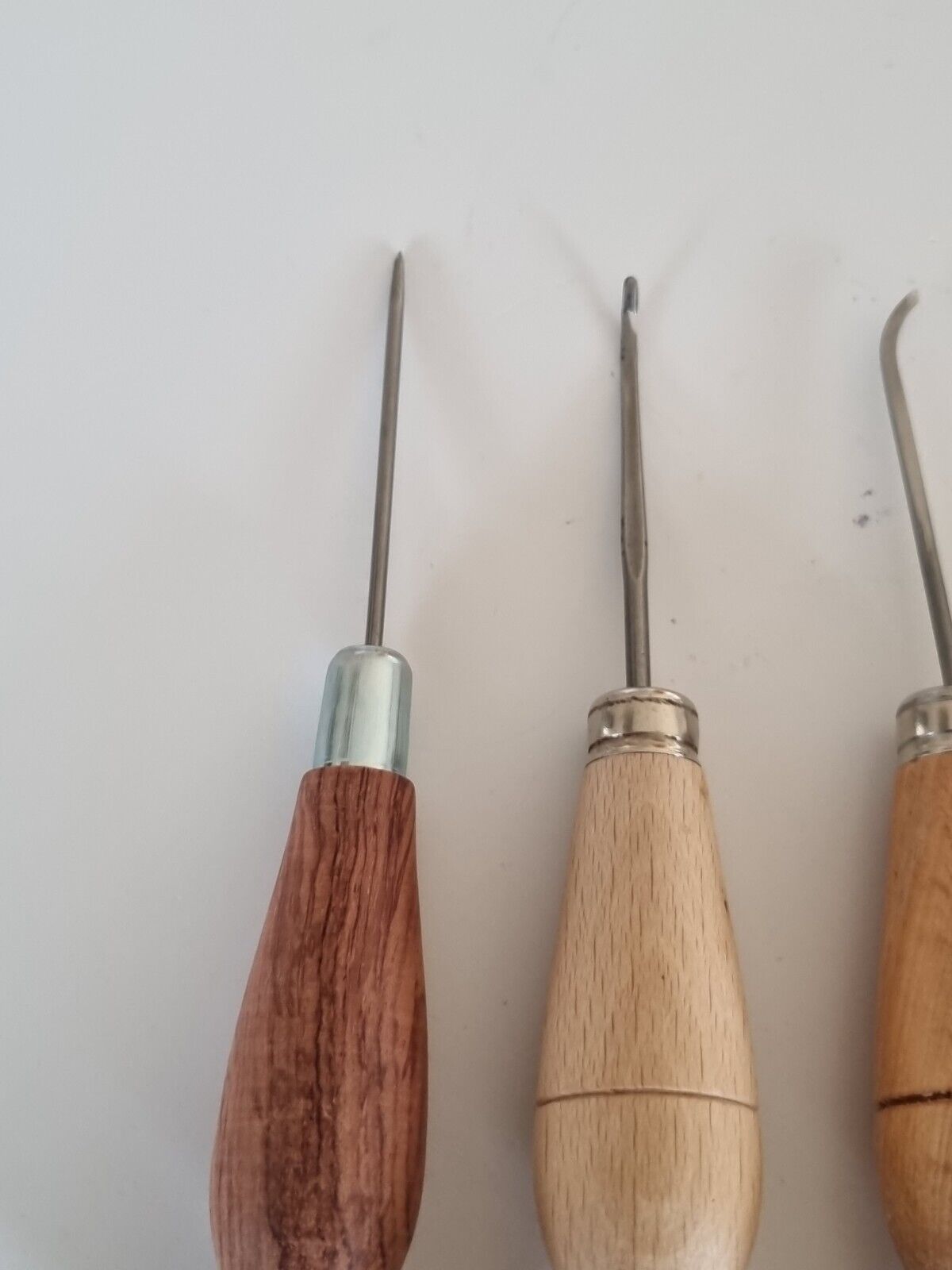 Closer view of the first 3 awls shown as straight, hooked and curved sole stitching awls all with wooden handles. Displayed against white background