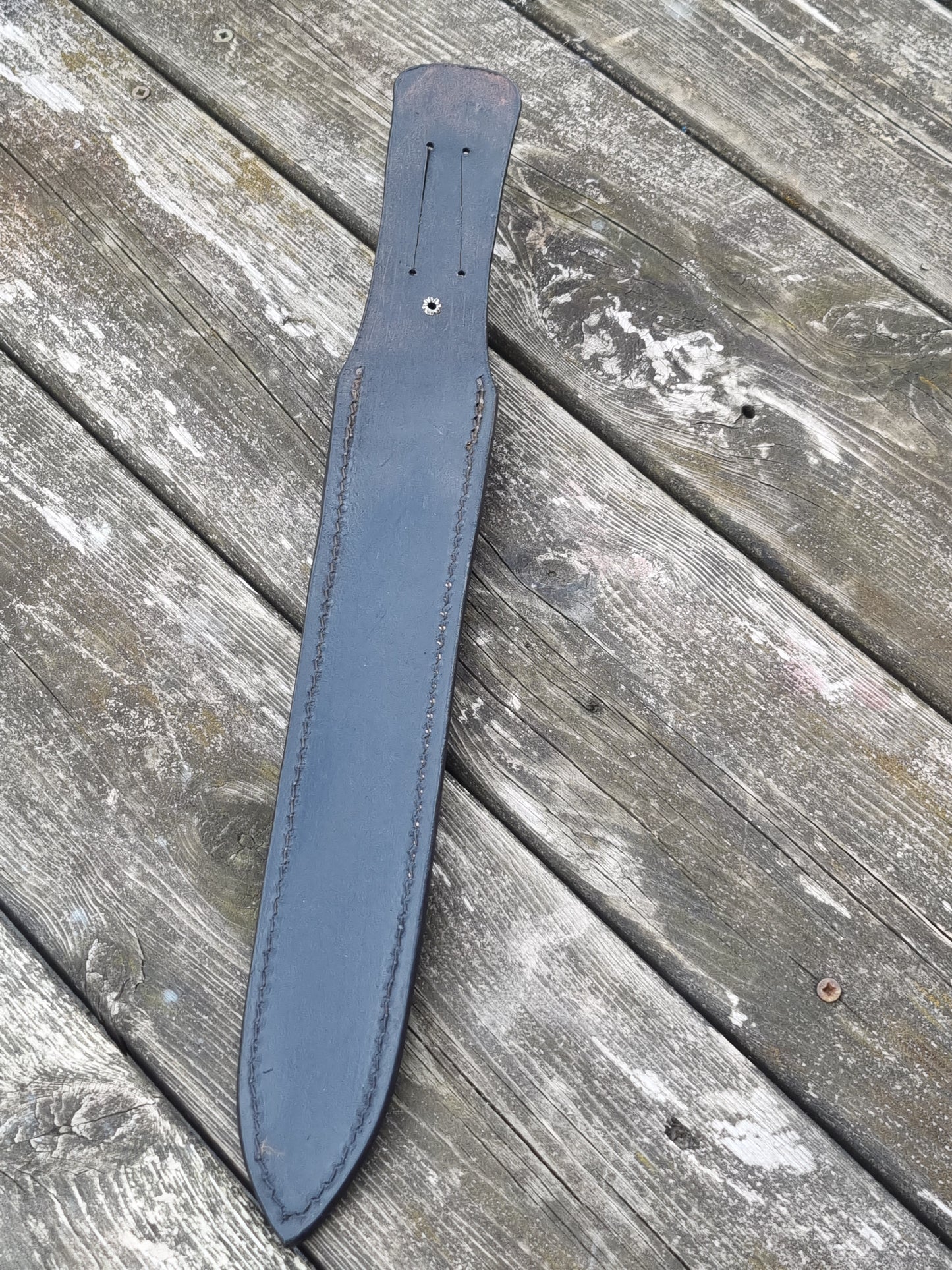 Showing back view of black leather sheath with belt slot on a wooden surface