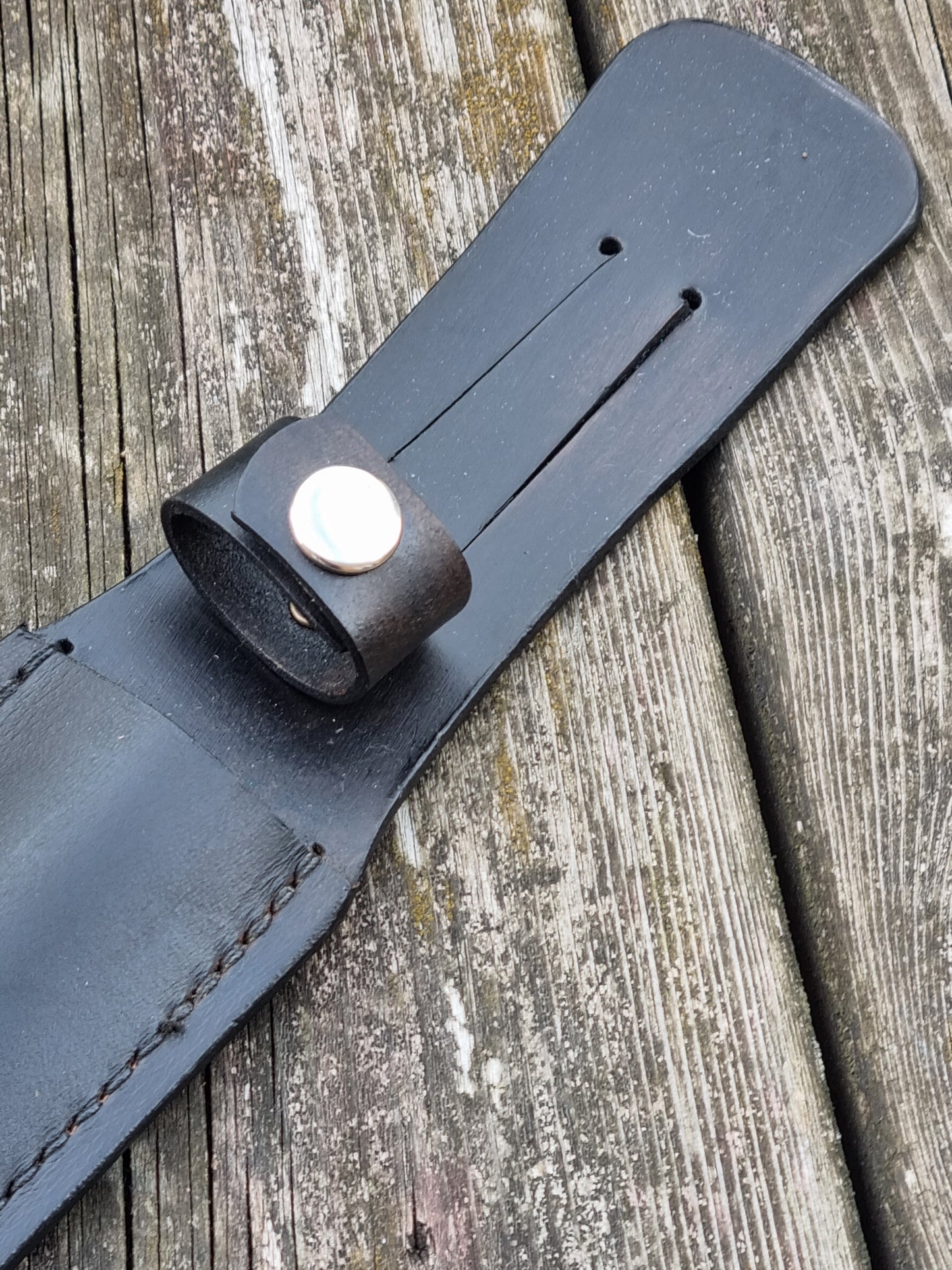 Close-up of a black leather sheath strap with belt slot and a handle snap loop  on a wooden surface