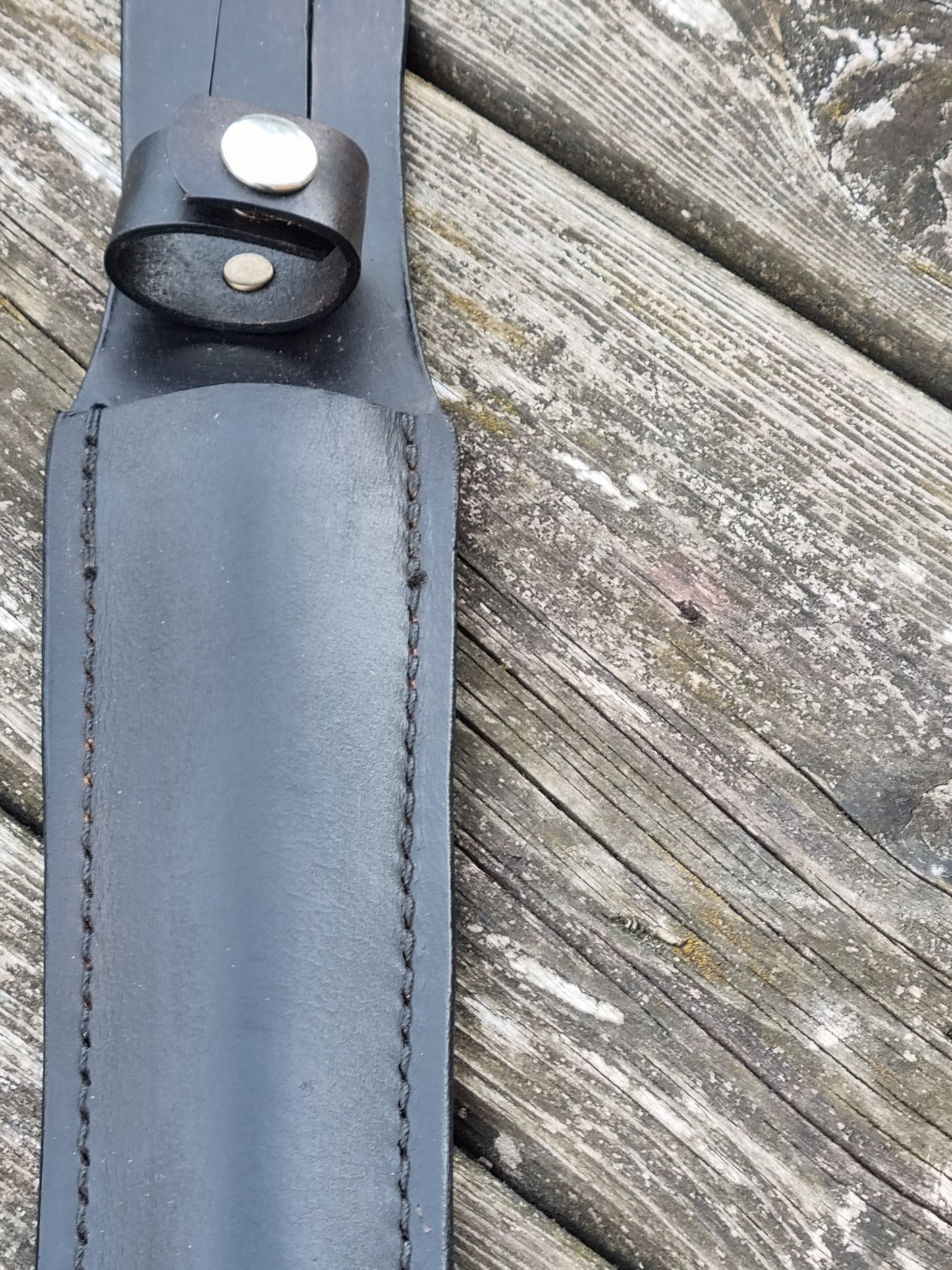 Close-up of a black leather sheath strap with a handle snap loop  on a wooden surface