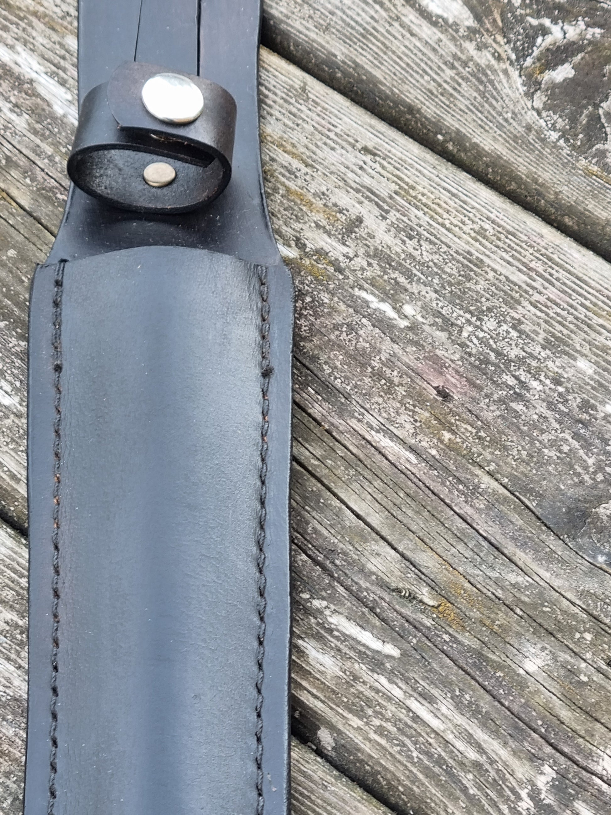 Close-up of a black leather sheath strap with a handle snap loop  on a wooden surface