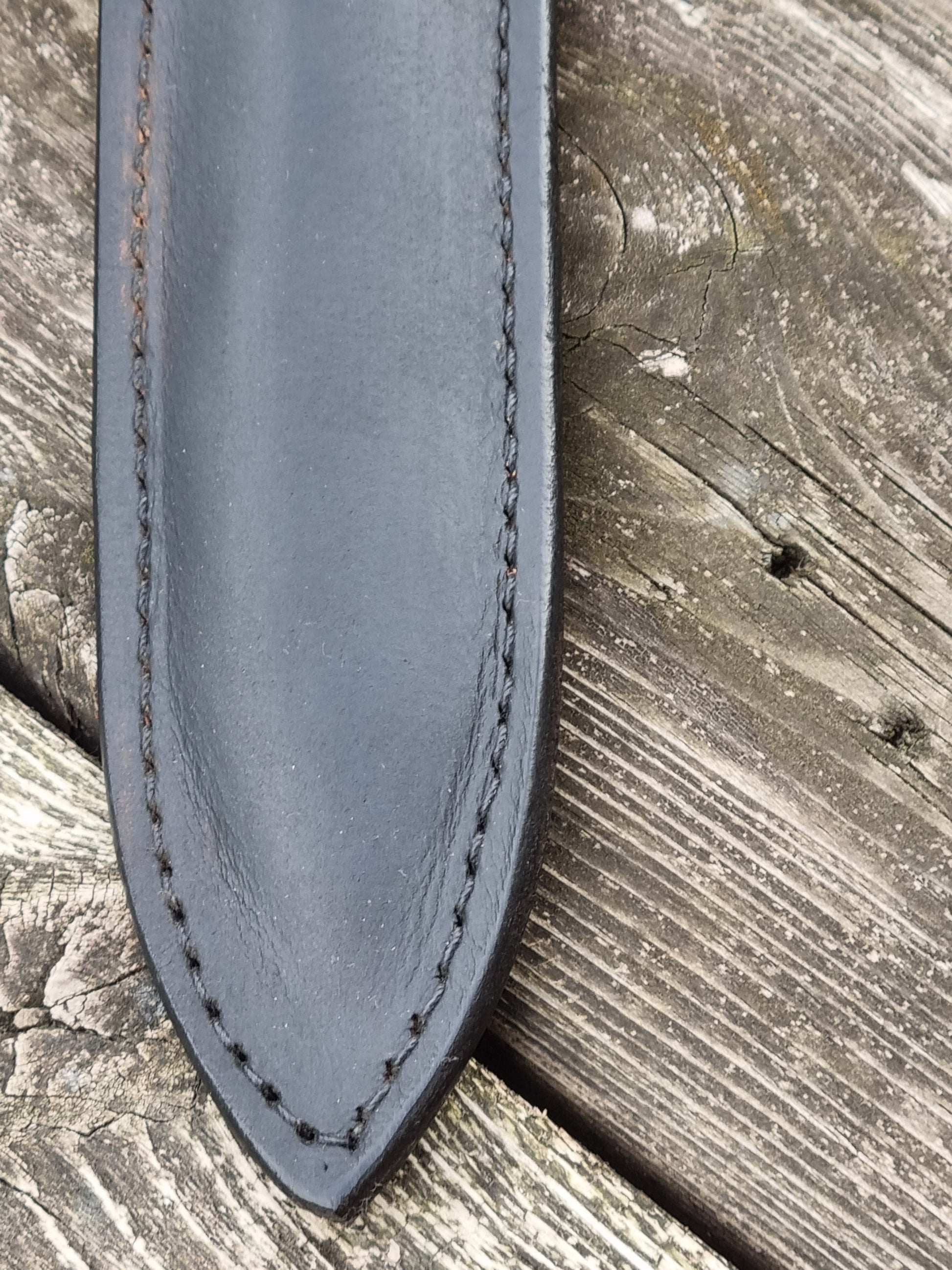 Close-up of a black  leather sheath tip with stitching on a wooden background