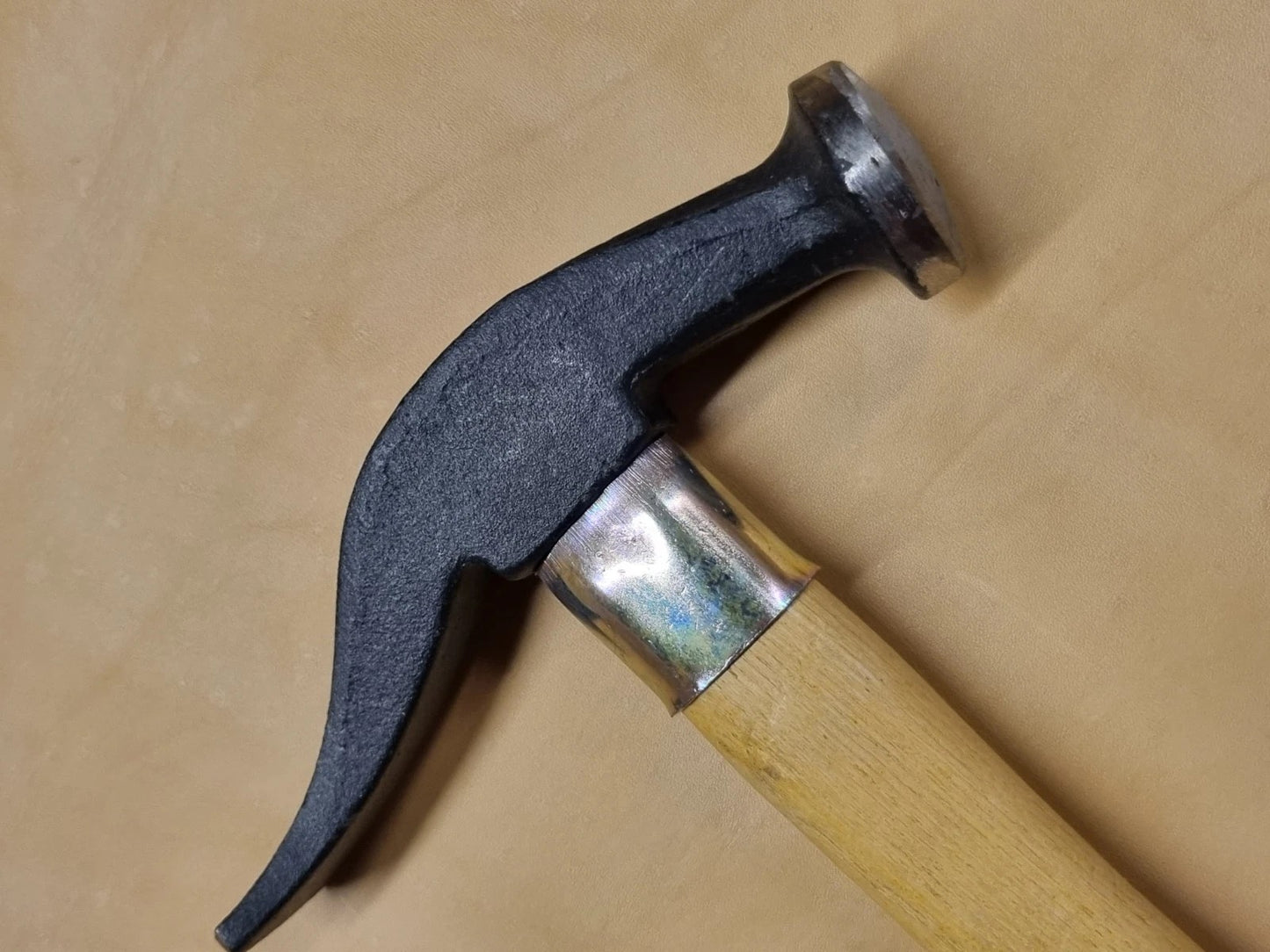 A close view of French hammer with a black metal head and a light wood handle, shown diagonally on a plain tan background.