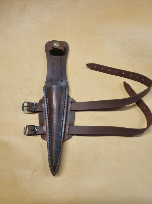 A brown leather sheath designed for a Fairbairn Sykes commando knife, displayed on a leather background.