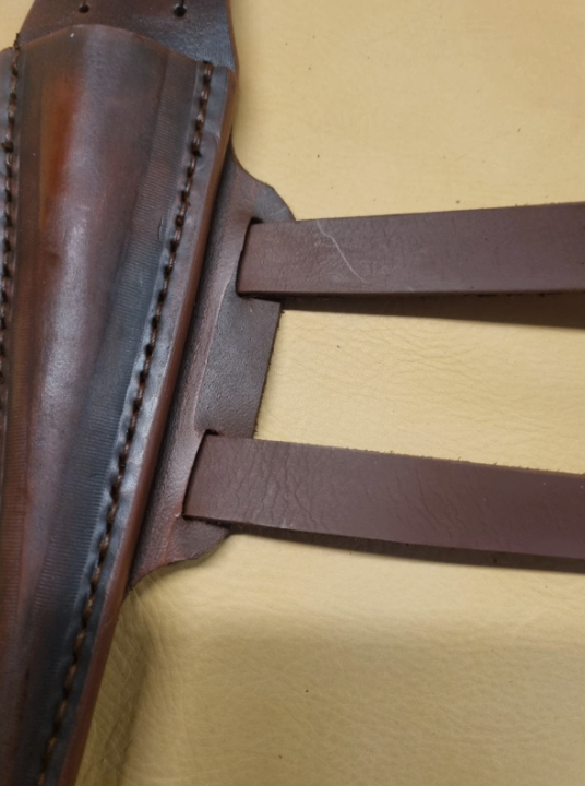 Close-up of a dark brown leather sheath with visible stitching and two attached straps, set against a pale yellow background.