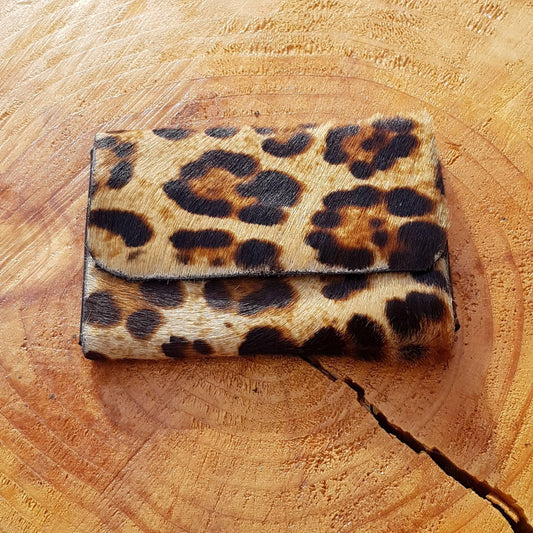A leopard print hair-on leather wallet displayed on a wooden surface.