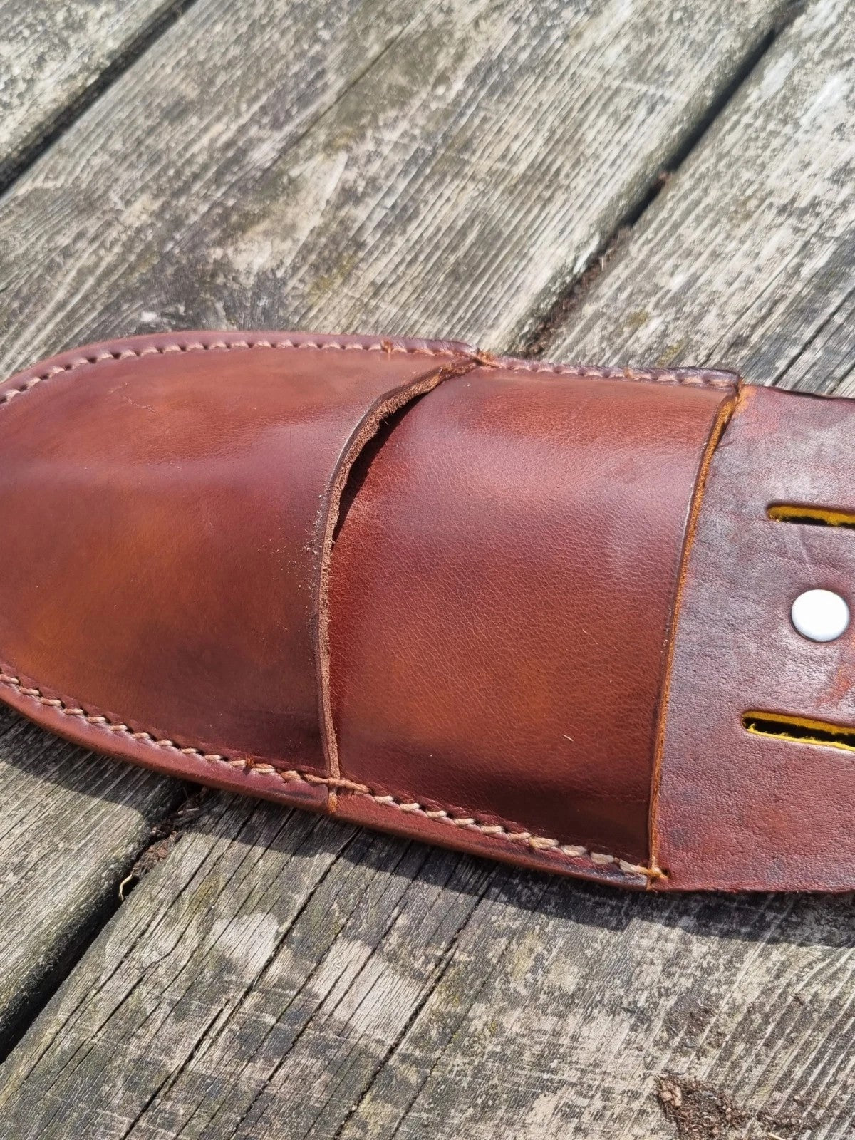 A close-up of a brown leather pruners sheath resting on weathered wooden planks.