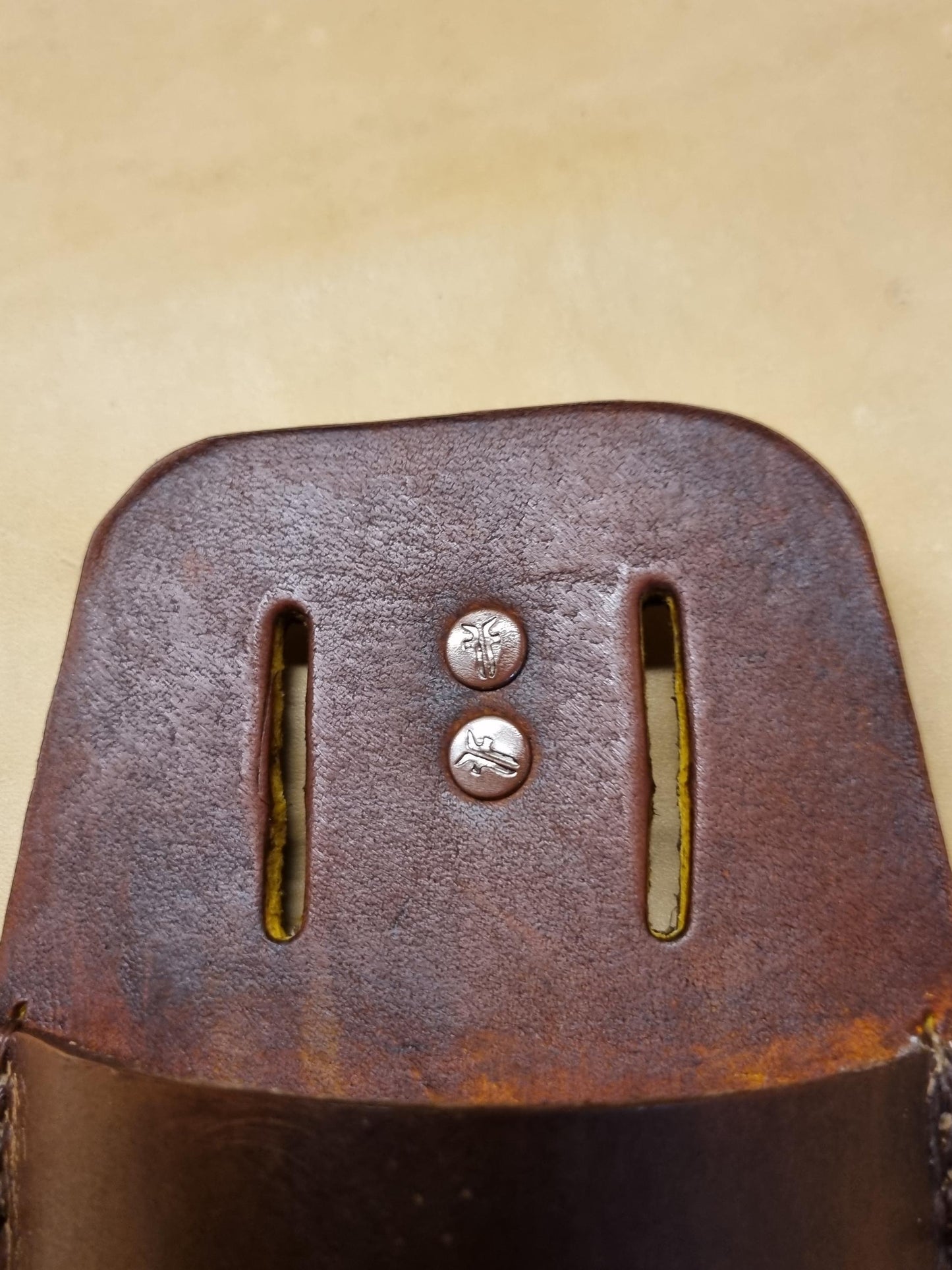 Close-up of a brown leather secateurs and pruners sheath showing belt slot with metal rivets, photographed against a light beige background.