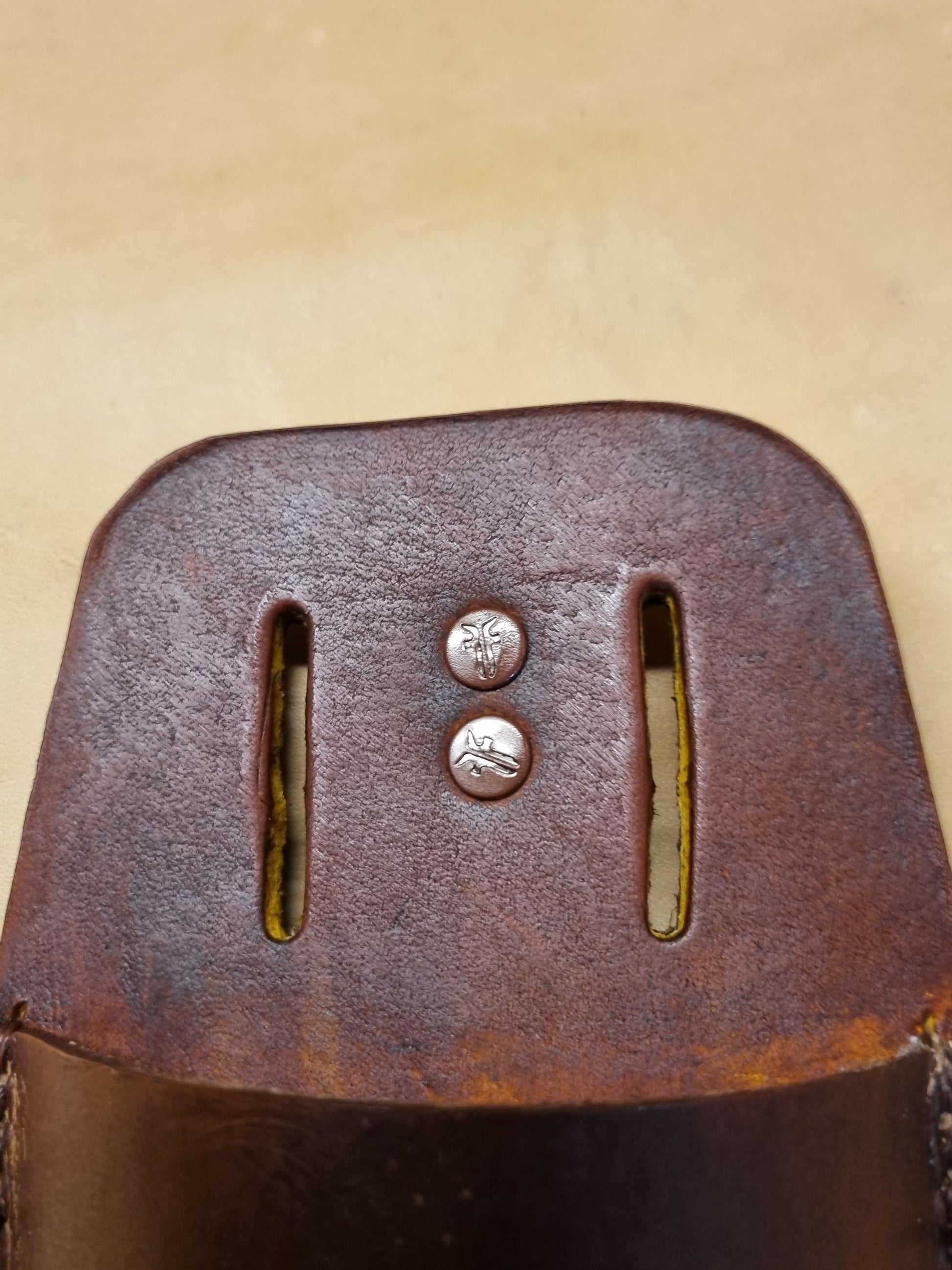 Close-up of a brown leather secateurs and pruners sheath showing belt slot with metal rivets, photographed against a light beige background.