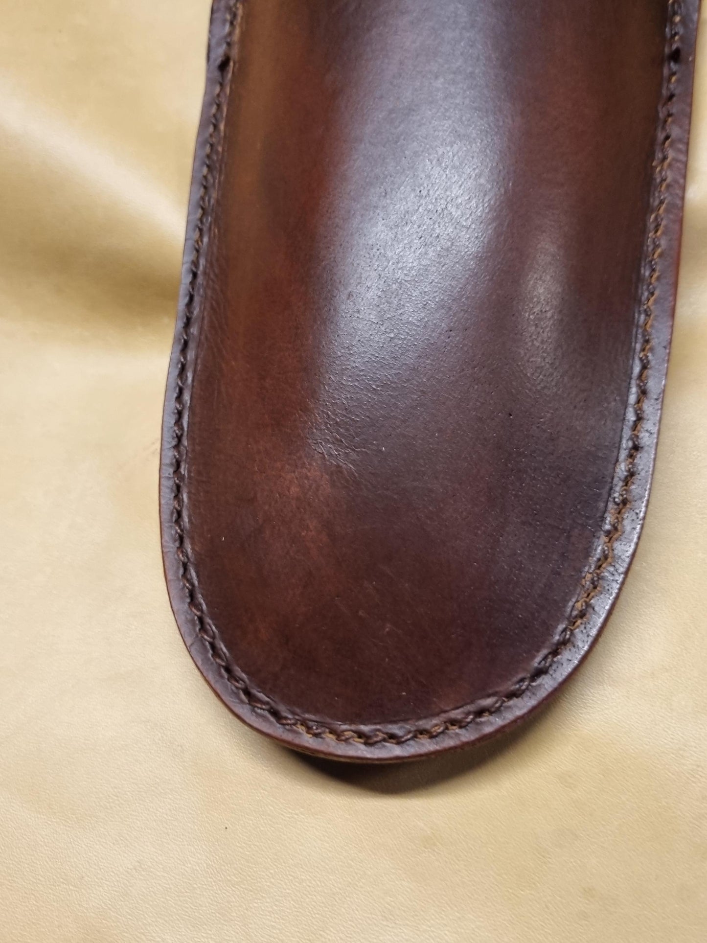 A dark brown moulded leather sheath for gardening pruners, secateurs and wire cutters showing detail stitch work around the nose of the sheath, displayed on a textured beige background.