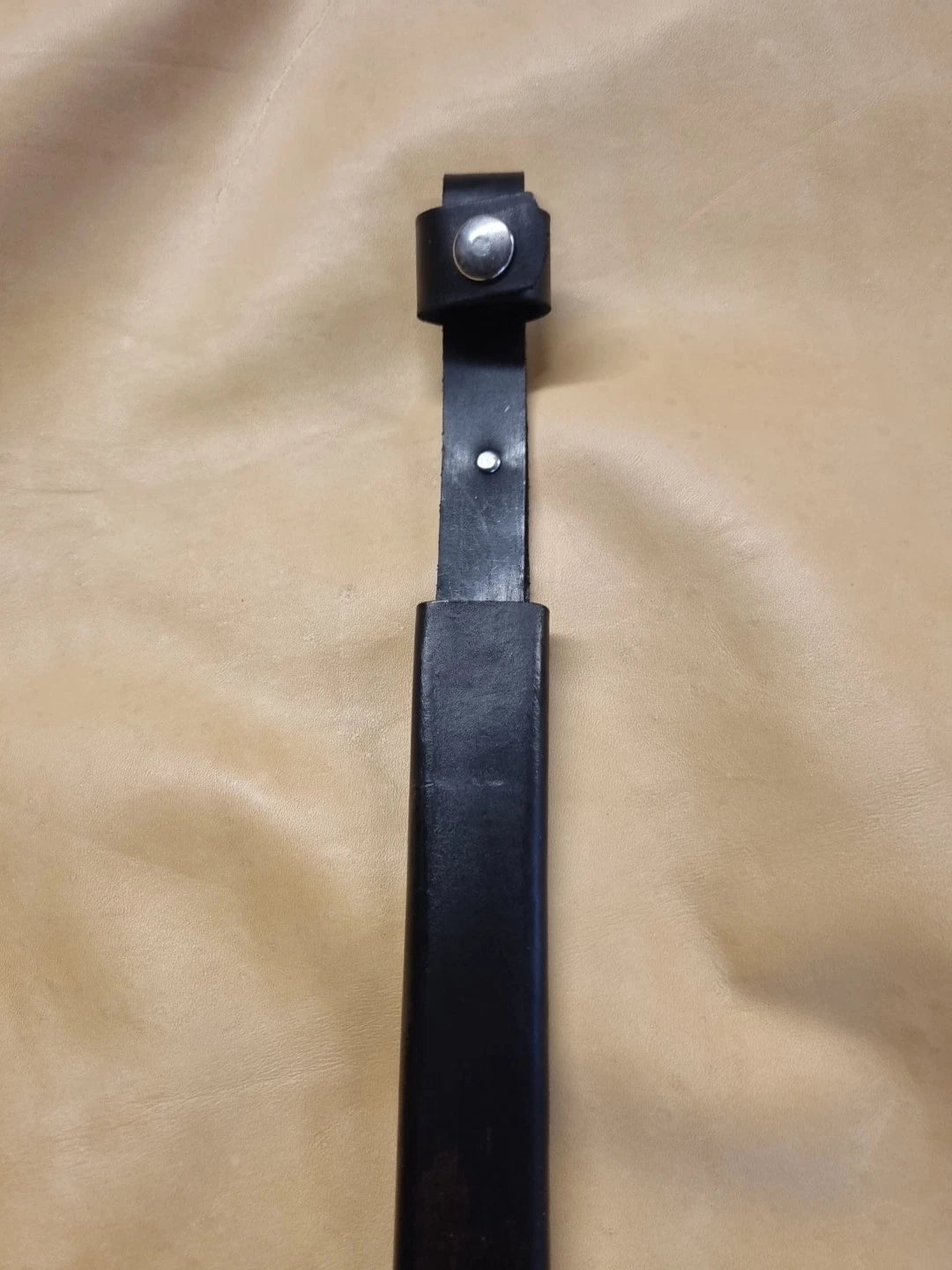 A black leather sheath for Hitler Youth knife for long blade with handle loop, shown on a beige fabric background.