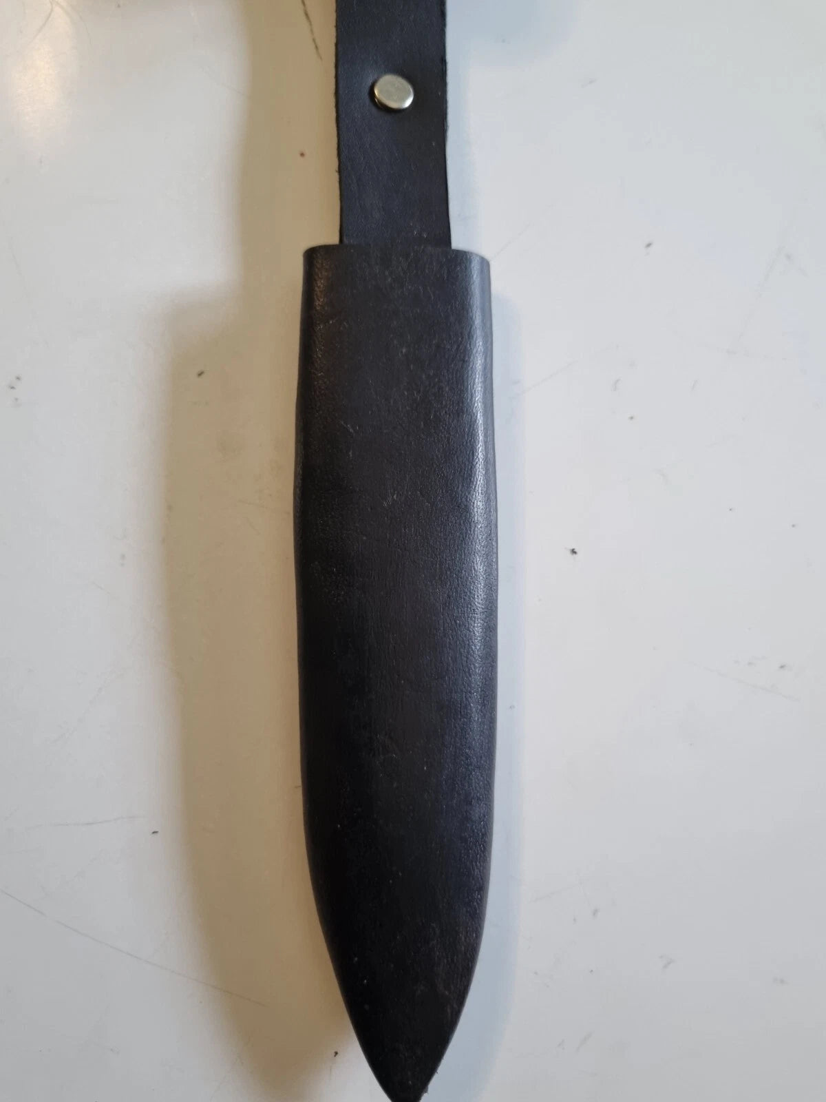 A black leather knife sheath with a matching black handle and a silver metal rivet, shown on a light off-white background.