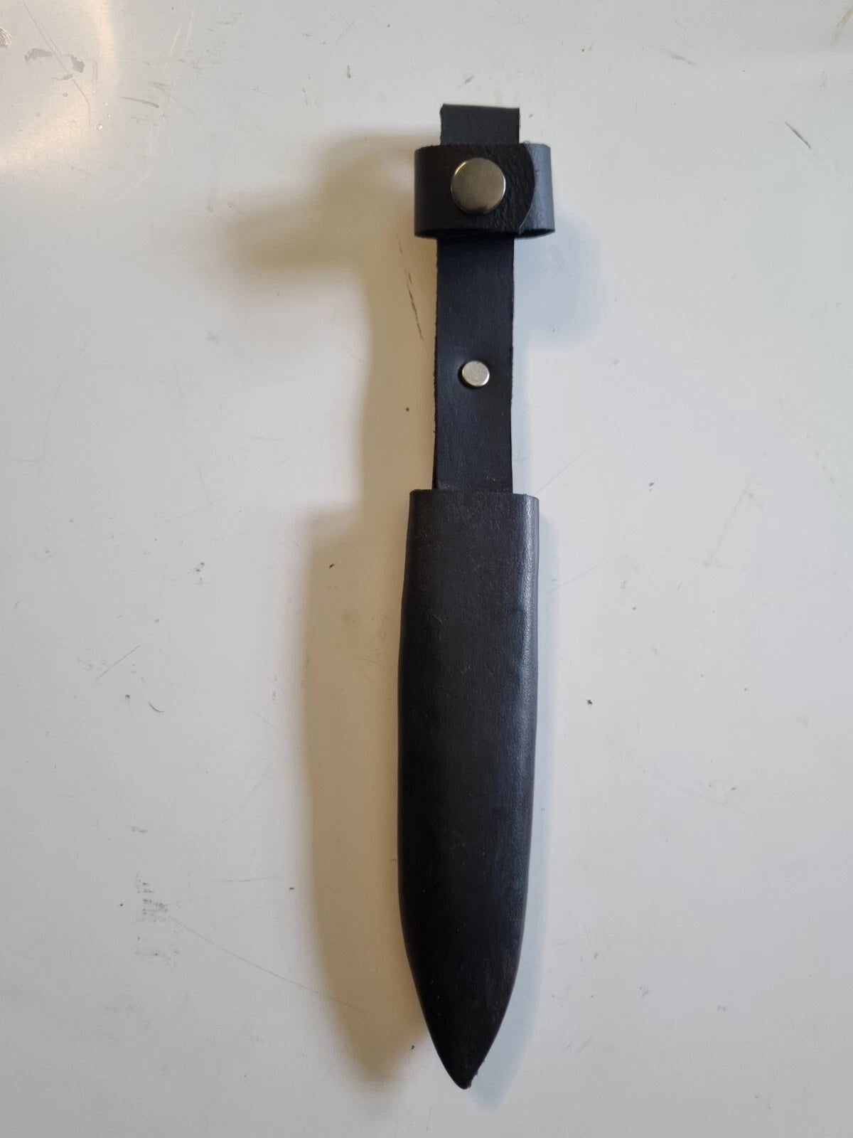 A black leather Hitler Youth knife sheath with a pointed tip and a snap-button closure, shown on a light off-white surface.