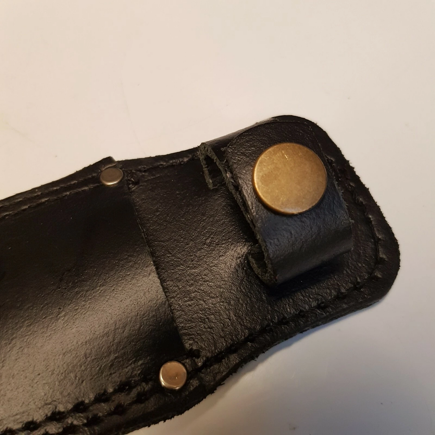 Close view of black leather Pentagon SOG sheath showing snap closer on white background
