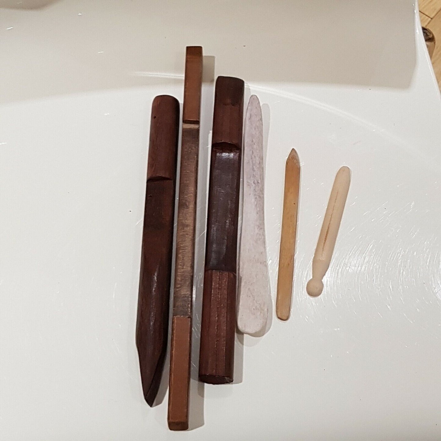 A set of 3 wooden burnishing tools along with cow bone and 2 small wooden scribers displayed on white back ground