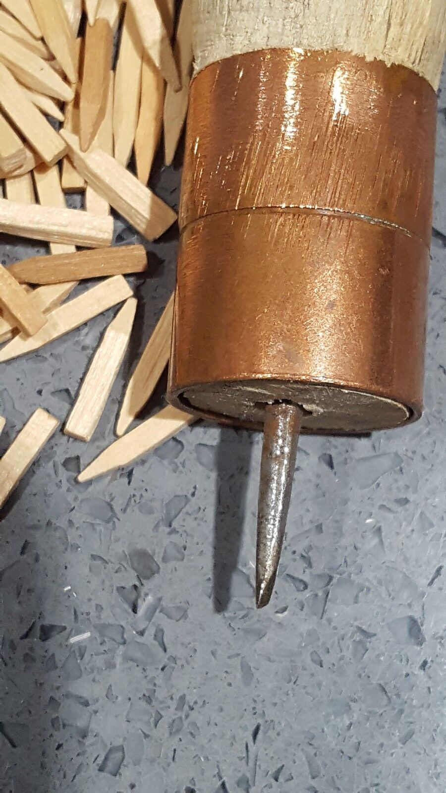 A close view of wooden handle with brass ferrules and sharp awl needle for driving wooden pegs or nails into leather shown next to heap of wooden pegs against grey background