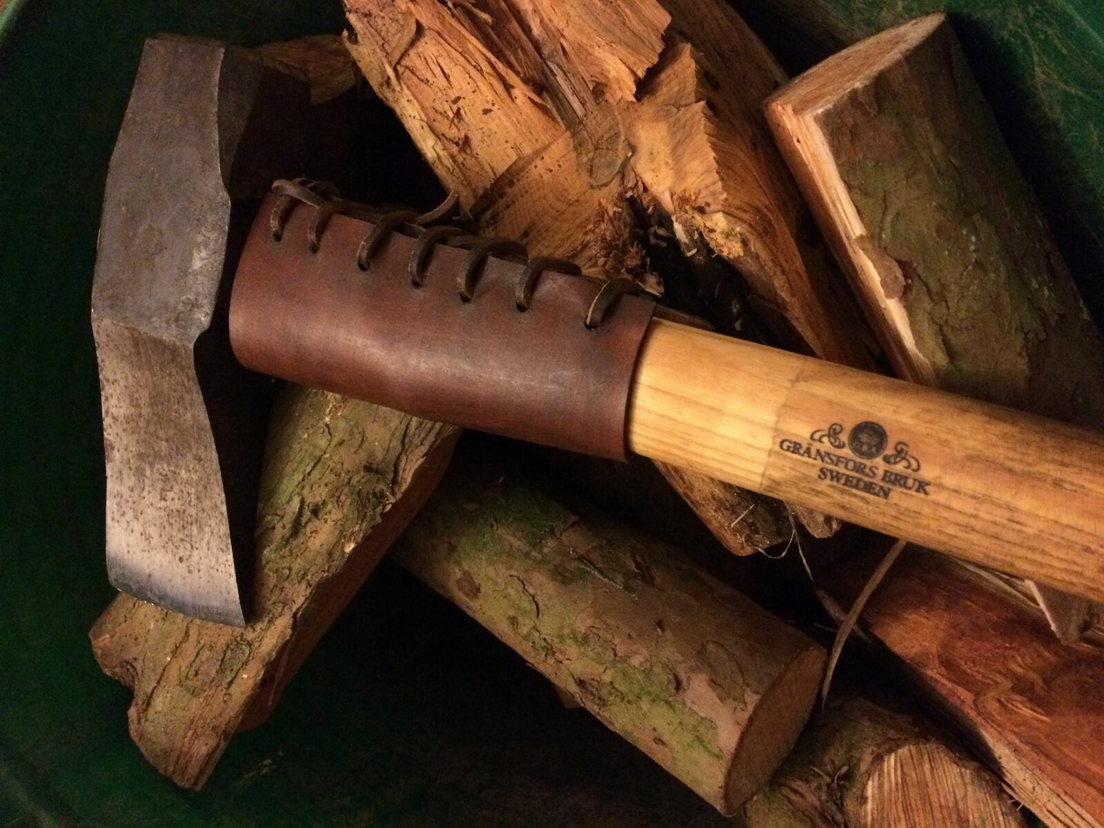 hand held axe with brown leather handle guard displayed on wooden logs background