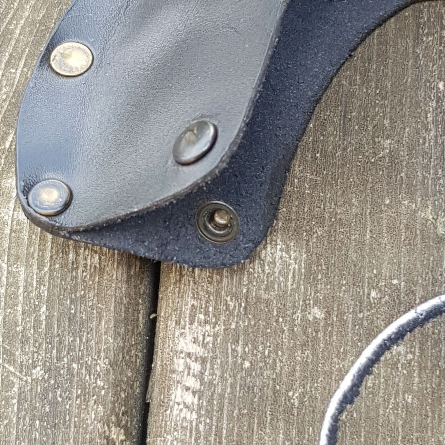 Close up view of axe head leather sheath displayed on a wooden surface.