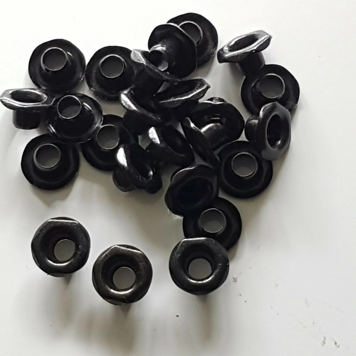 A pile of small black plastic grommet-like hardware pieces with circular centers and ring-shaped openings, photographed on a plain white surface.