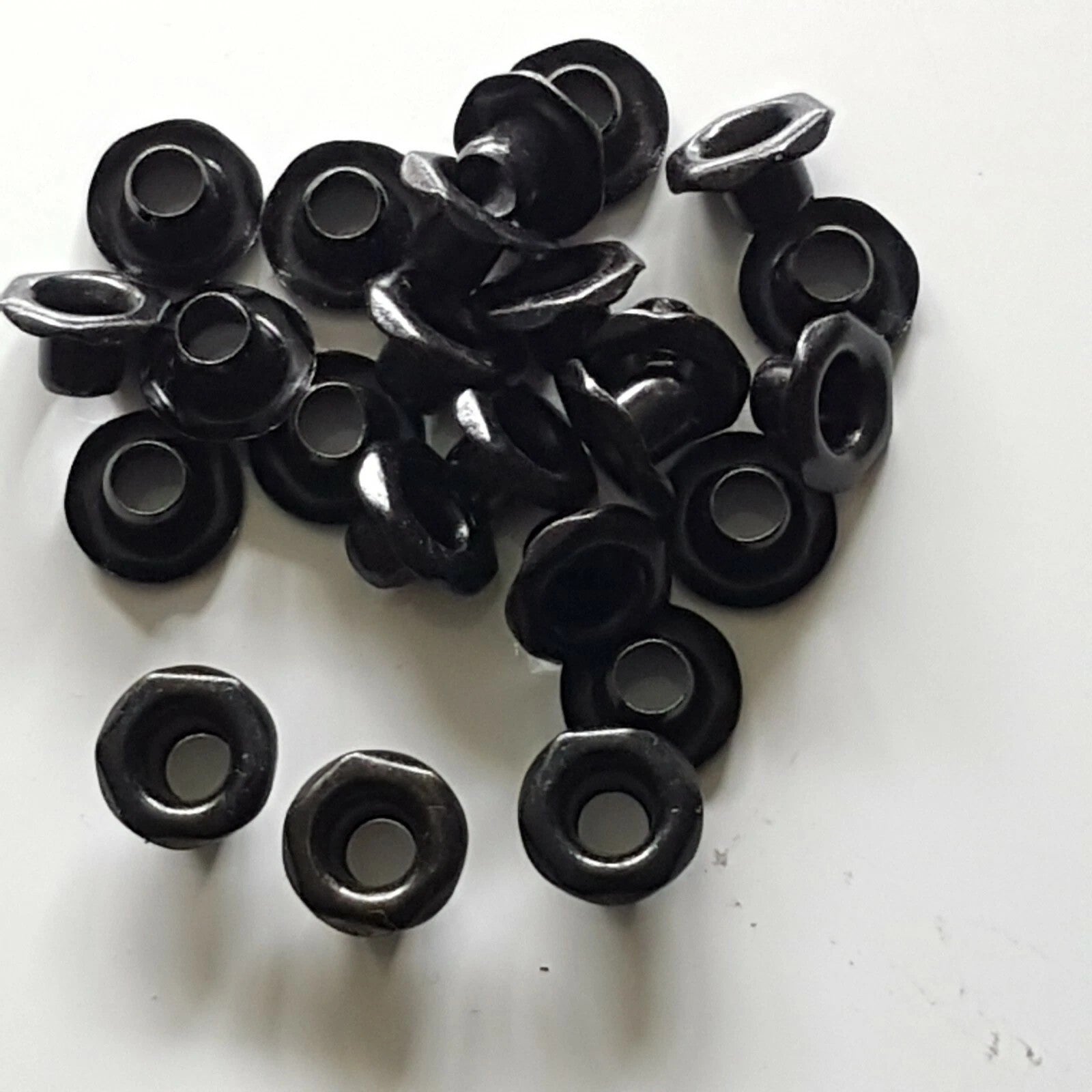 A pile of small black plastic grommet-like hardware pieces with circular centers and ring-shaped openings, photographed on a plain white surface.