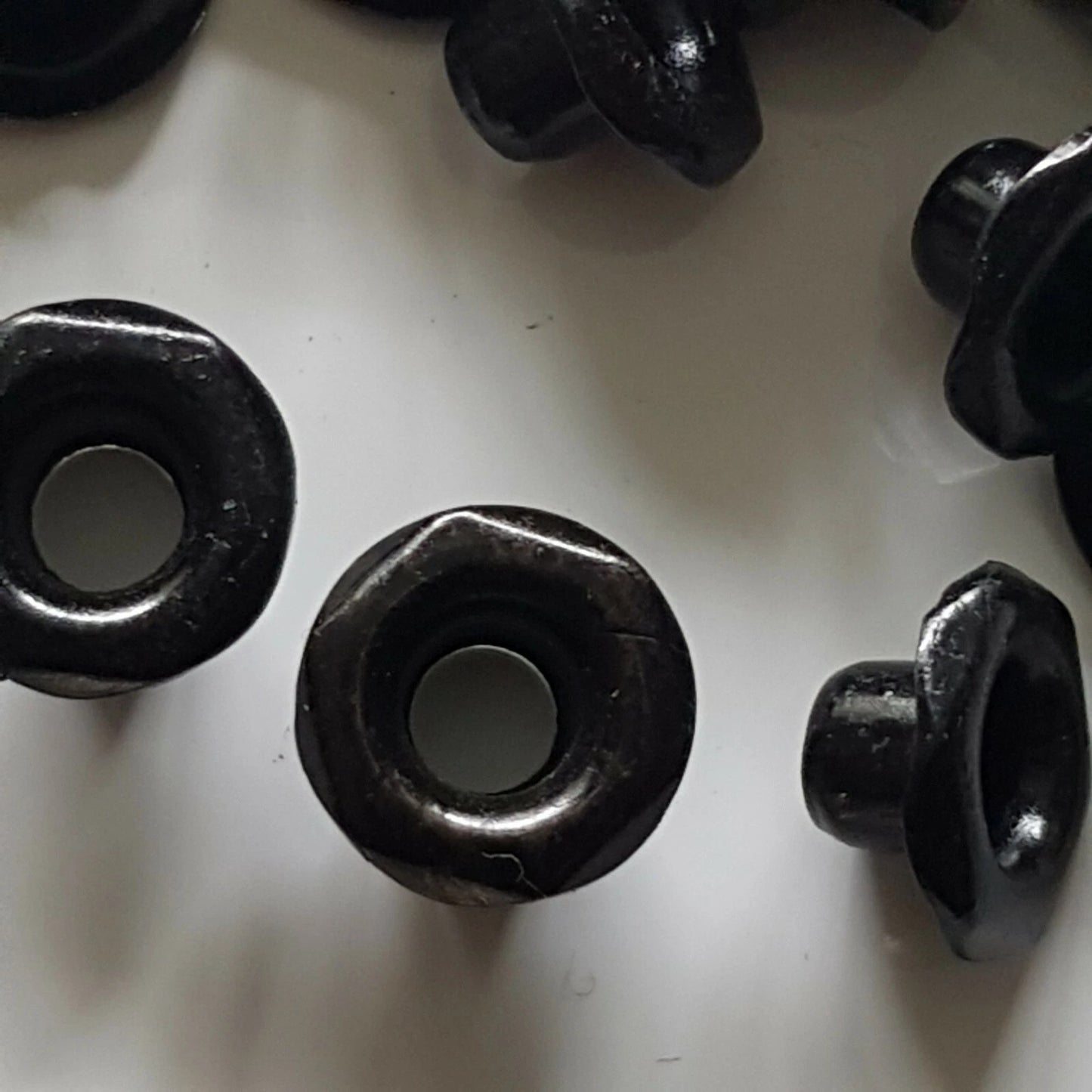 Several black plastic eyelets or grommet-like hardware pieces arranged on a plain white surface.