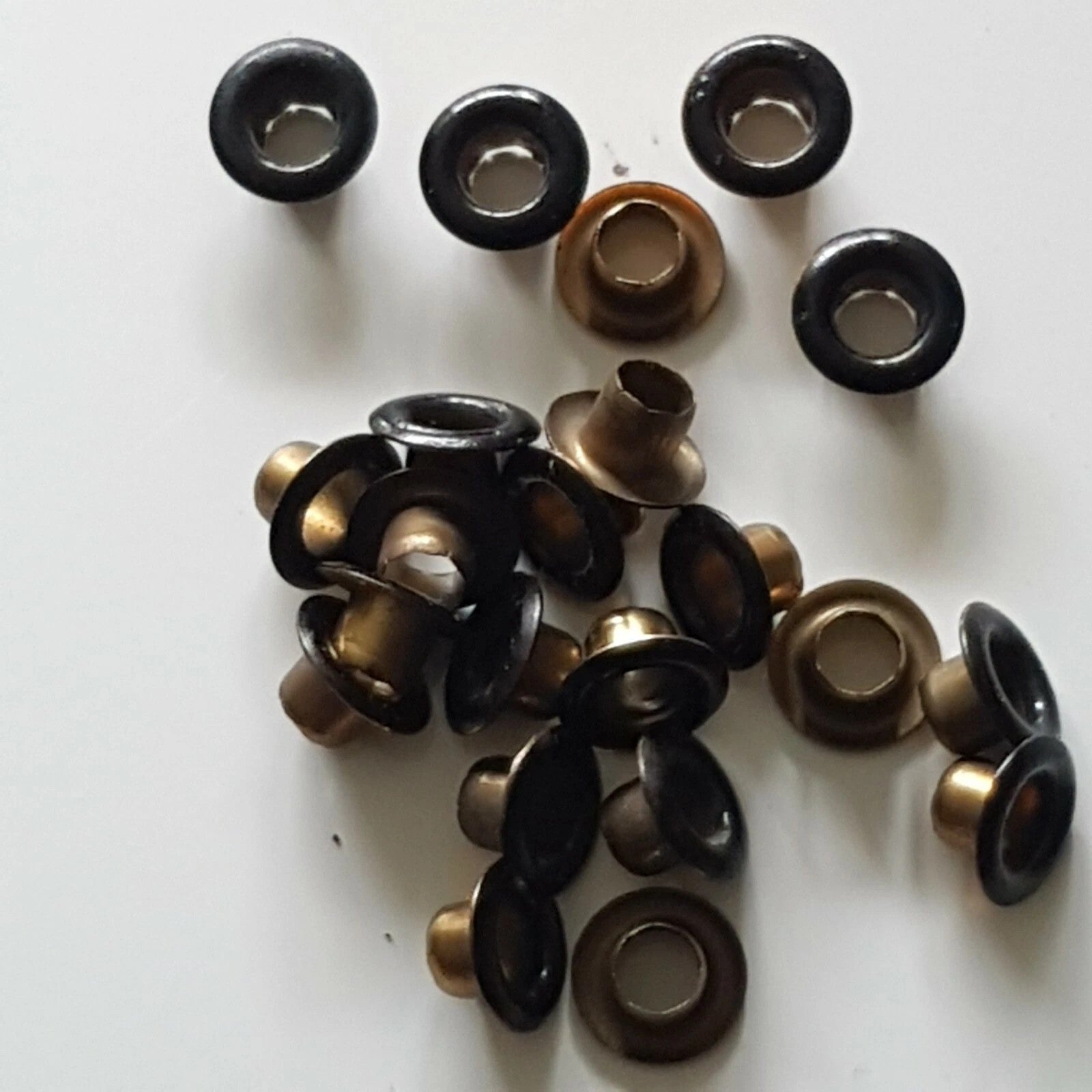 A pile of metal grommets and eyelets in black and antique bronze finishes, arranged on a plain white background.