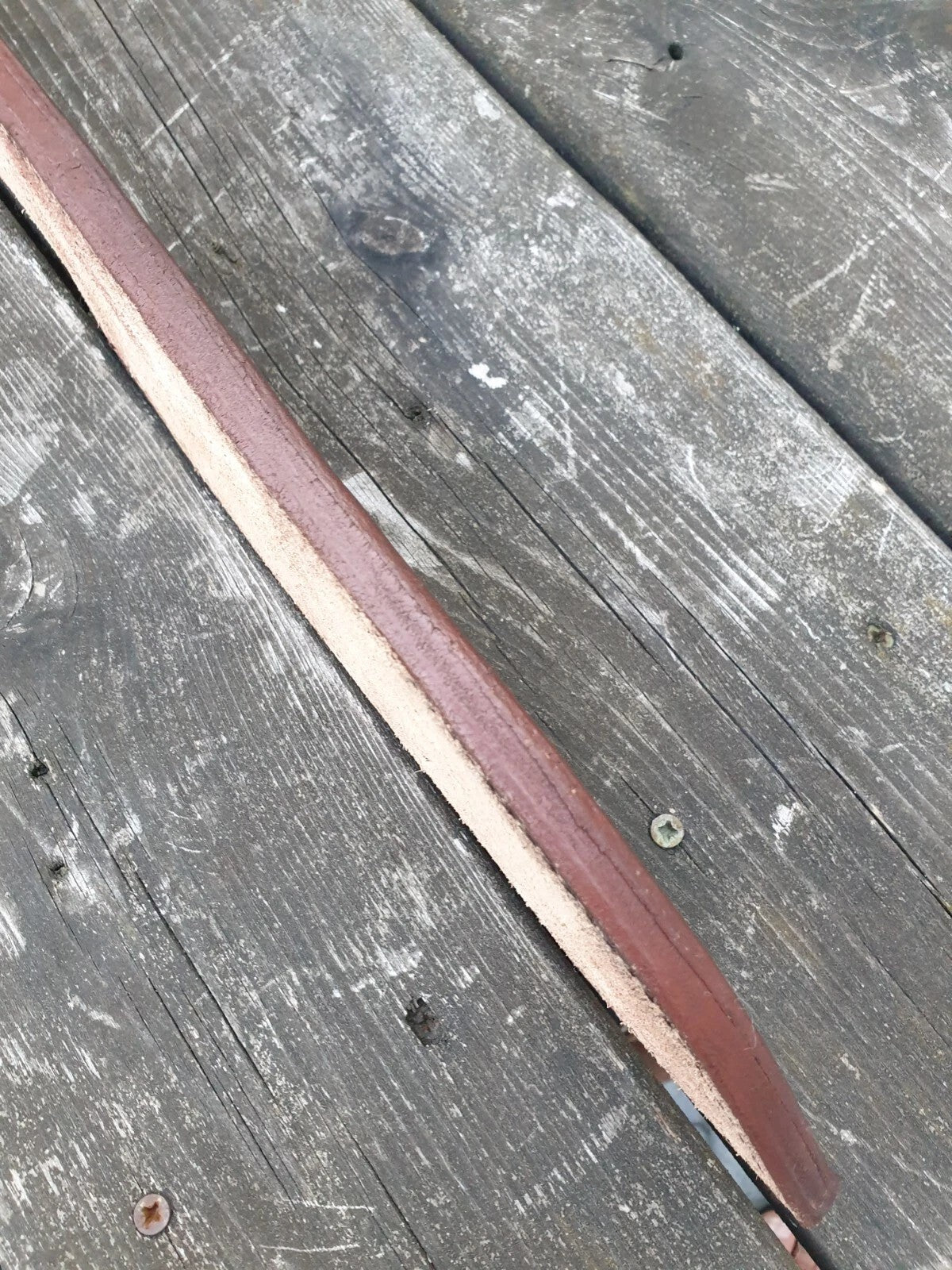 A close-up of a welted knife sheath  laid diagonally across weathered gray wooden planks.