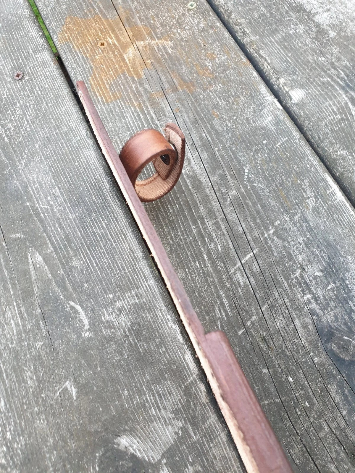 A handle loop made of leather, placed diagonally on a weathered gray wooden plank surface.