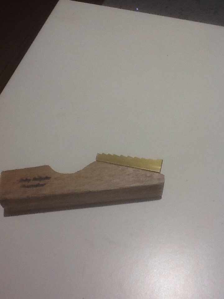 A side view of pure brass welt mill with a wooden base, showing the logo, brass steps and the groove for securing the welt.