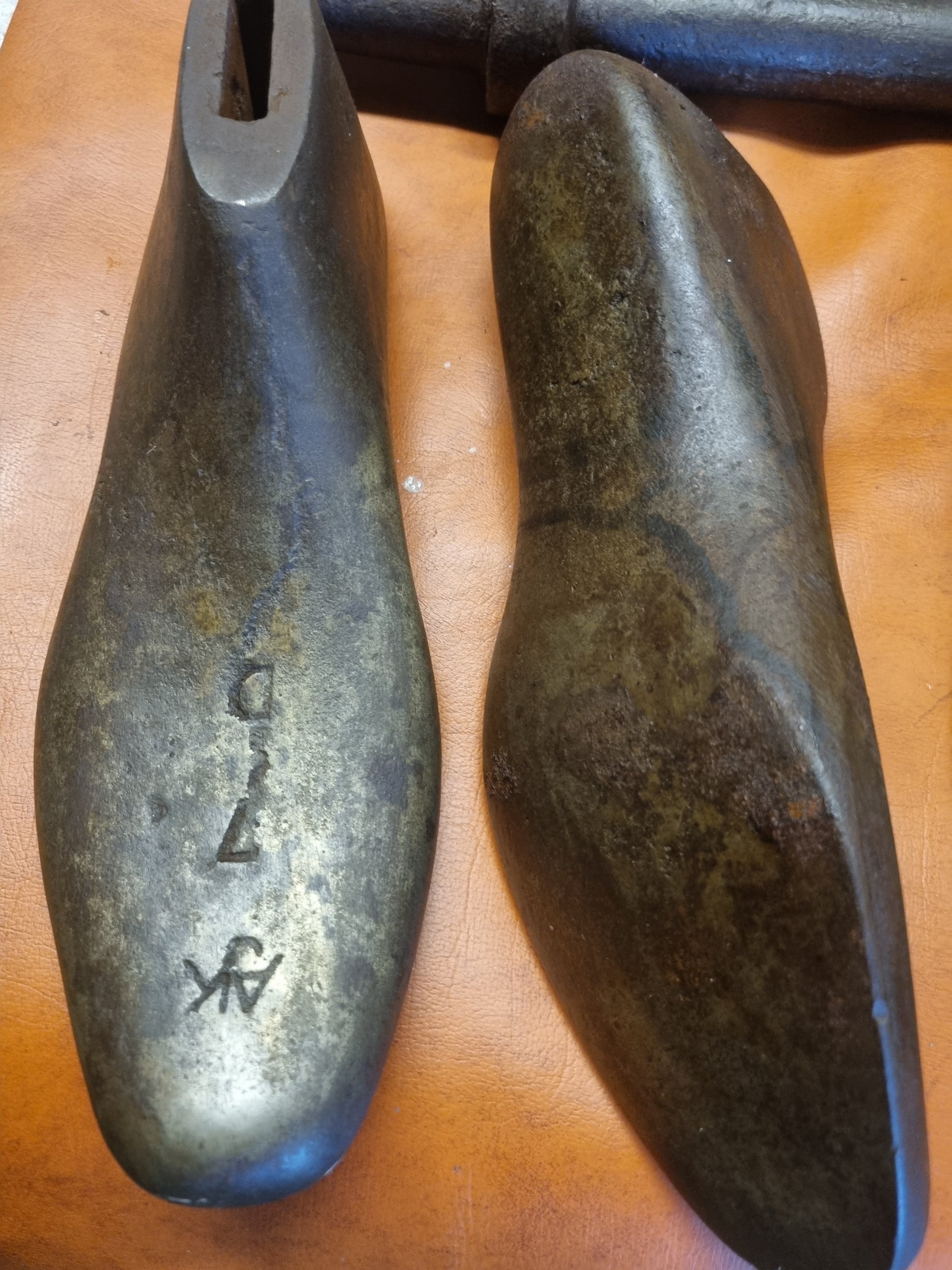 Two cast metal shoe lasts with printed letters AJK 7 C on a wooden surface
