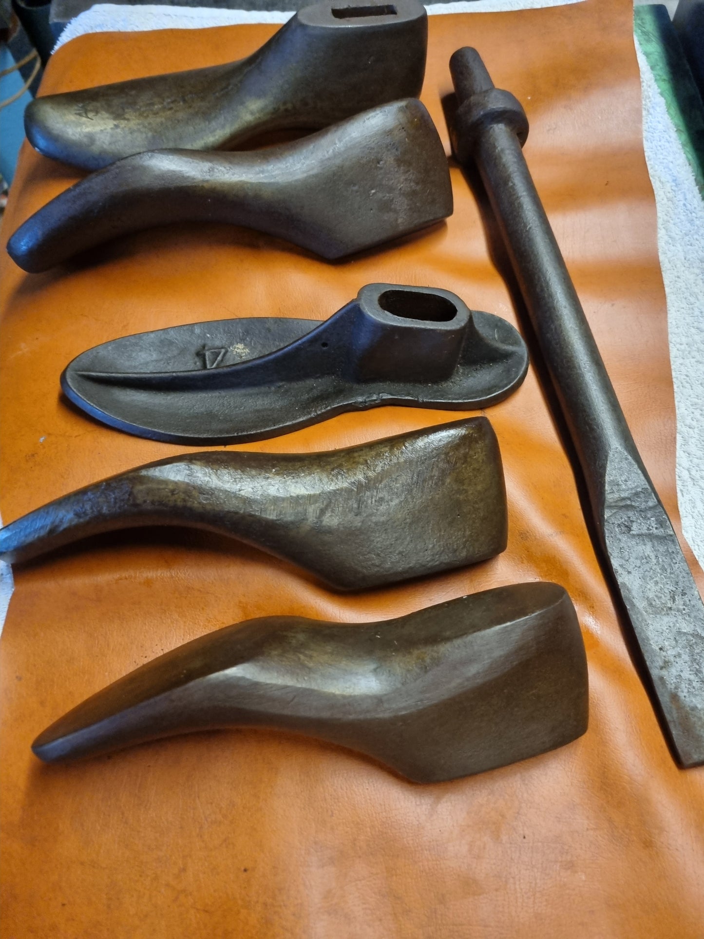 Set of 5 cast metal shoe lasts with long steel mounting rod on a brown leather surface