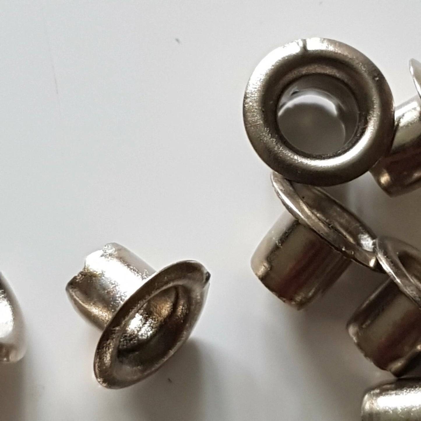 Several small metallic grommet-like hardware pieces with a silver-toned finish scattered on a plain light background.