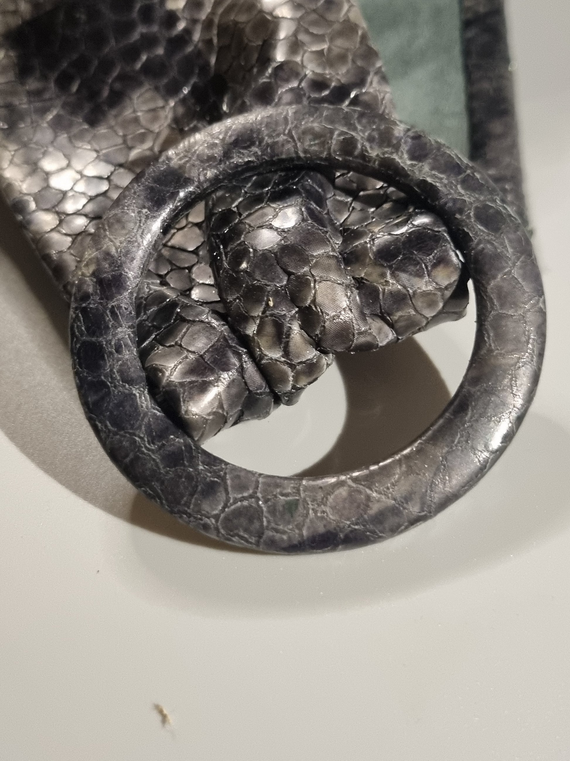 Close-up of a leather cover buckle with matching grey cobra embossed buckle, scale pattern on a light grey background.