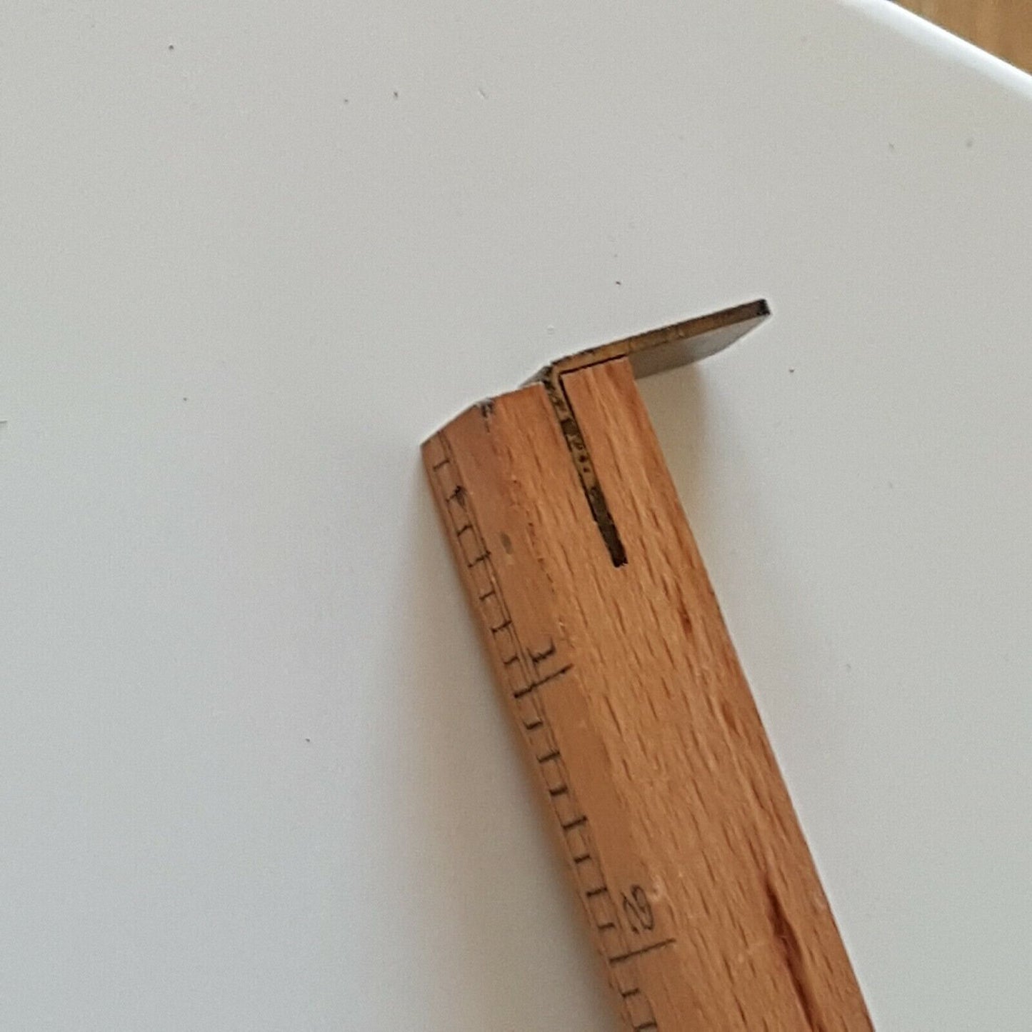 A close view of wooden cloggers shoe size stick showing one end with brass stopper place don a on a white surface.