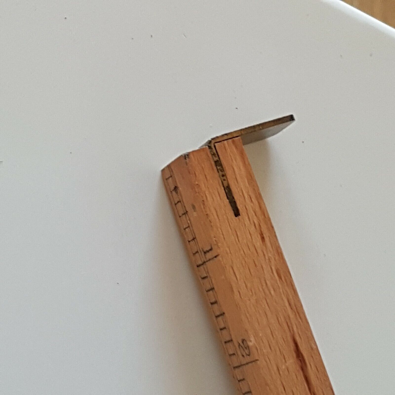 A close view of wooden cloggers shoe size stick showing one end with brass stopper place don a on a white surface.