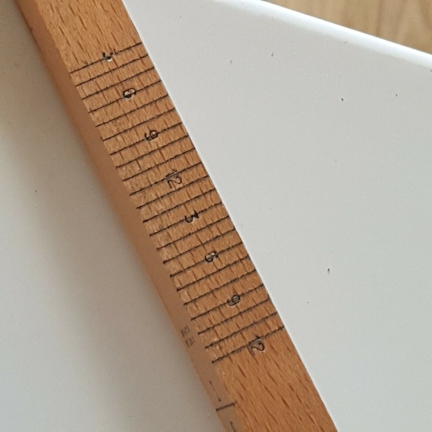 A close view of cloggers wooden stick with narrow scale showing numbers 3 to 12, placed on a white surface.