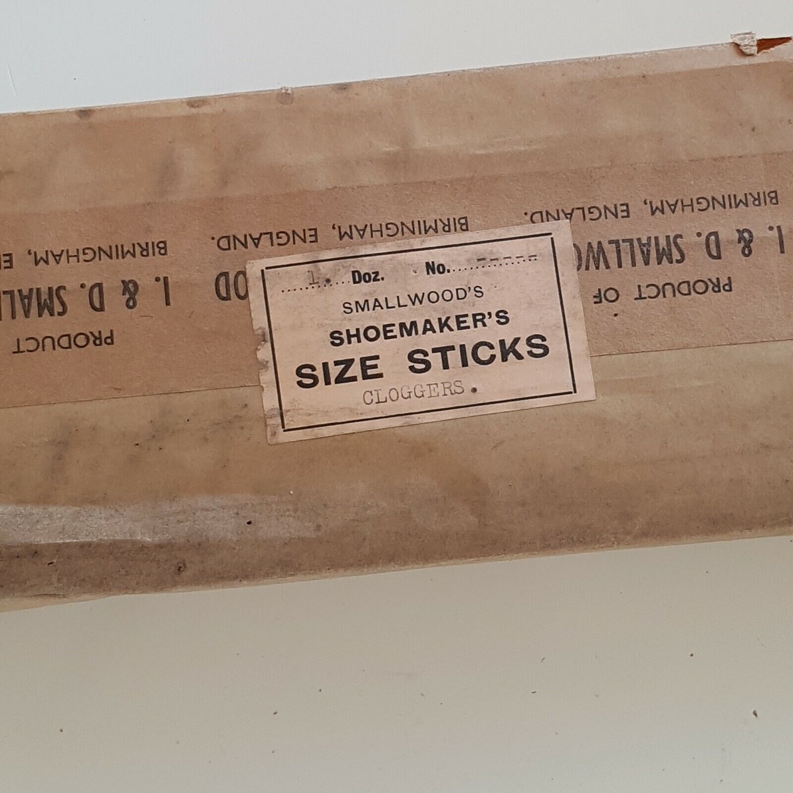 Close view of wooden shoe size stick with makers name Smallwoods SHOEMAKERS SIZE STICKS - Cloggers, placed on a white surface.