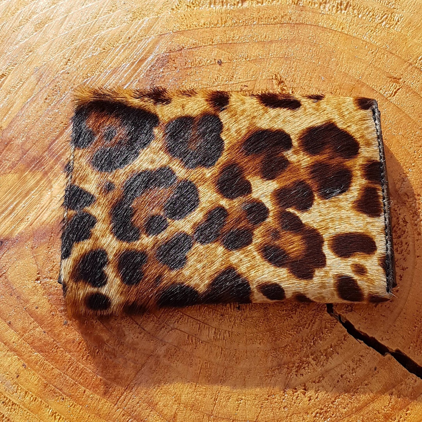 Close up view of leopard print hair-on leather wallet displayed on a wooden surface.