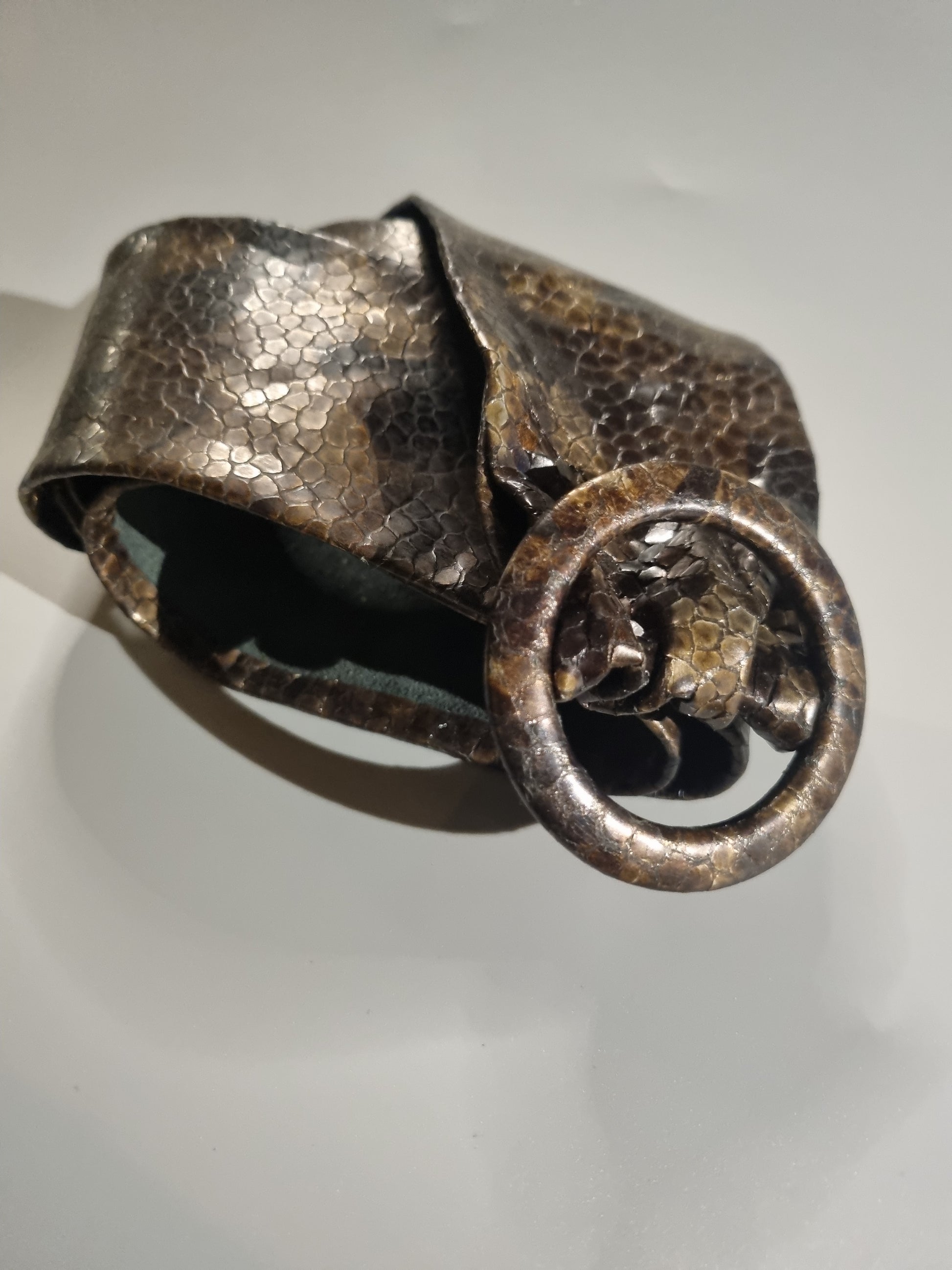 A hammered metal cuff bracelet with a large circular ring buckle featuring a textured animal head detail, shown on a plain light background.