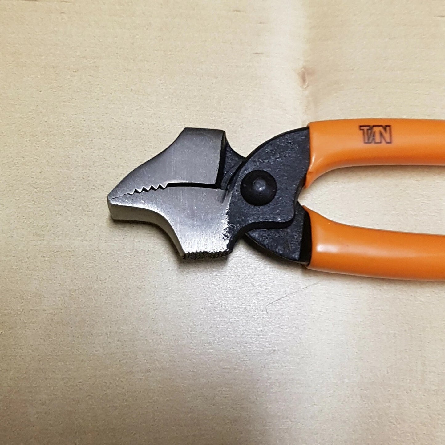 A pair of shoe lasting pliers with orange handles and a silver metal jaw, placed on a light beige textured surface