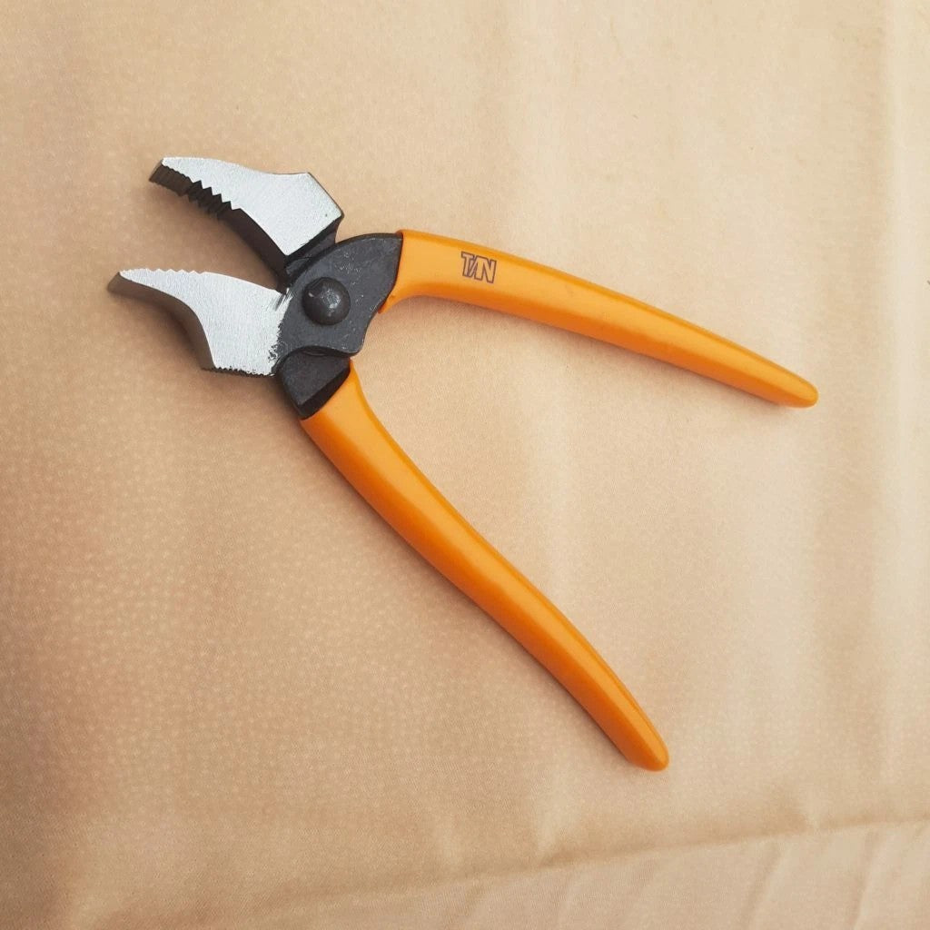 Orange-handled curved nose lasting pliers with silver metal jaw heads for pulling leather over shoe last, placed on a beige textured surface.
