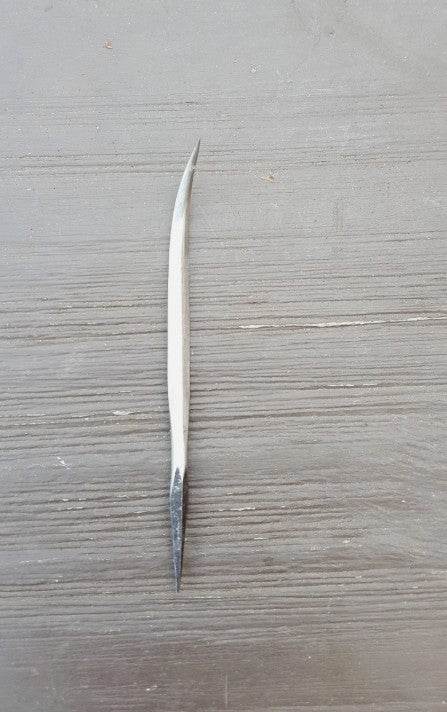 A single long, slender metal tool with a pointed tip lies vertically on a gray wood-grain surface.